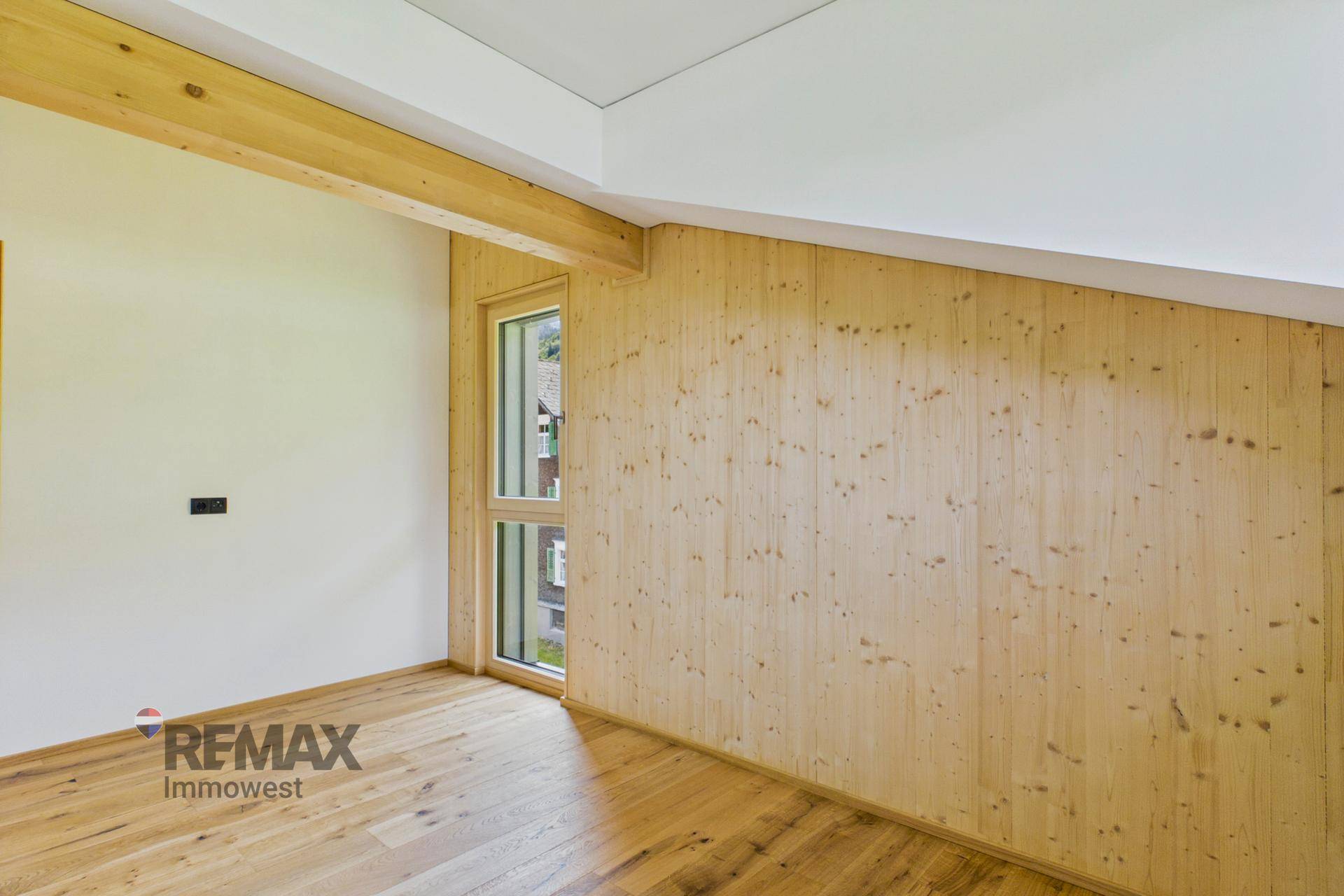 Helles Zimmer mit Holzvertäfelung, Holzbalken und schrägem Dach im Dachgeschoss.