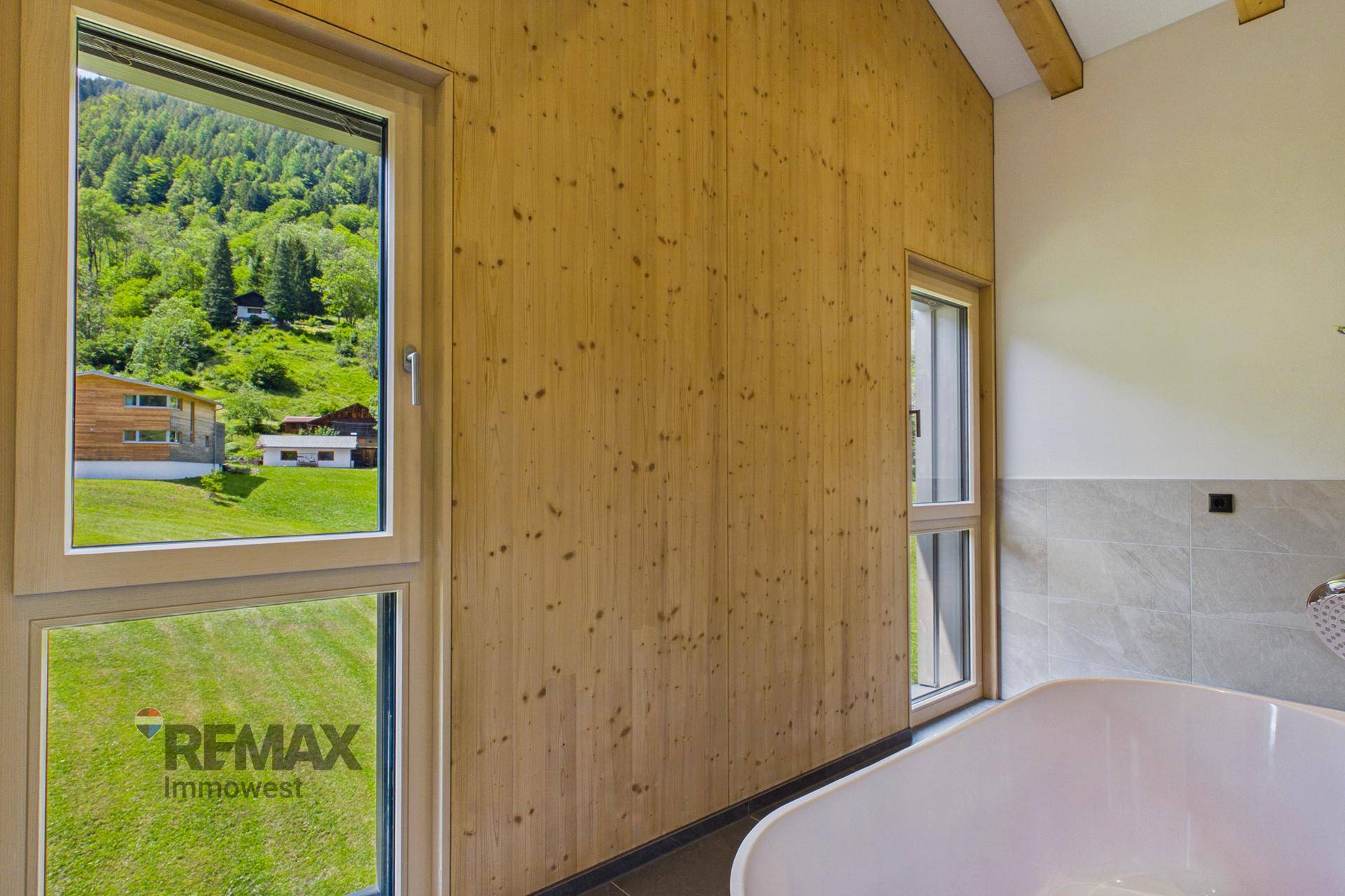 Helles Badezimmer mit Holzverkleidung, Fenster und Blick auf die grüne Landschaft.