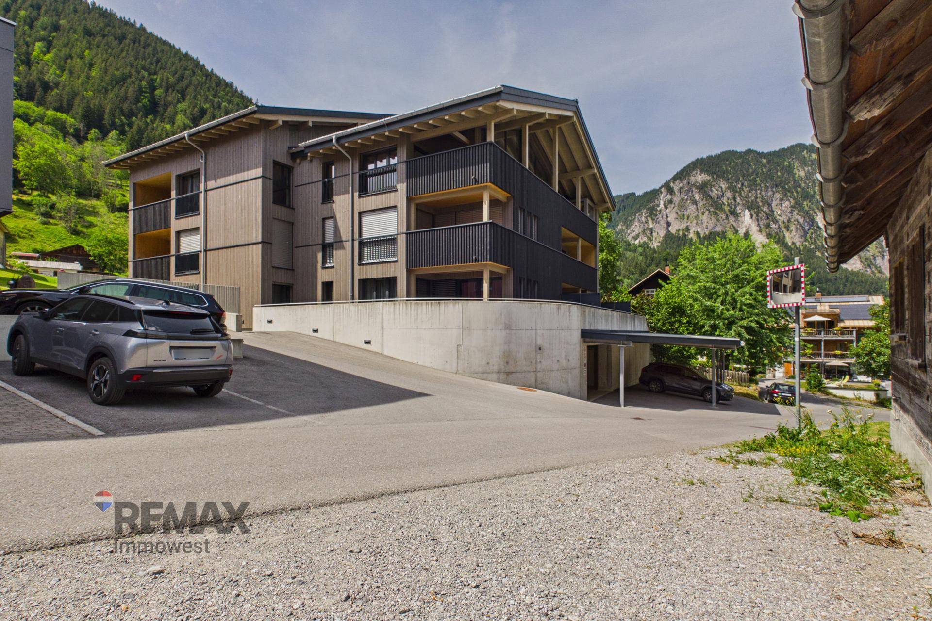 Modernes Gebäude mit Balkonen und Carport in alpiner Berglandschaft.