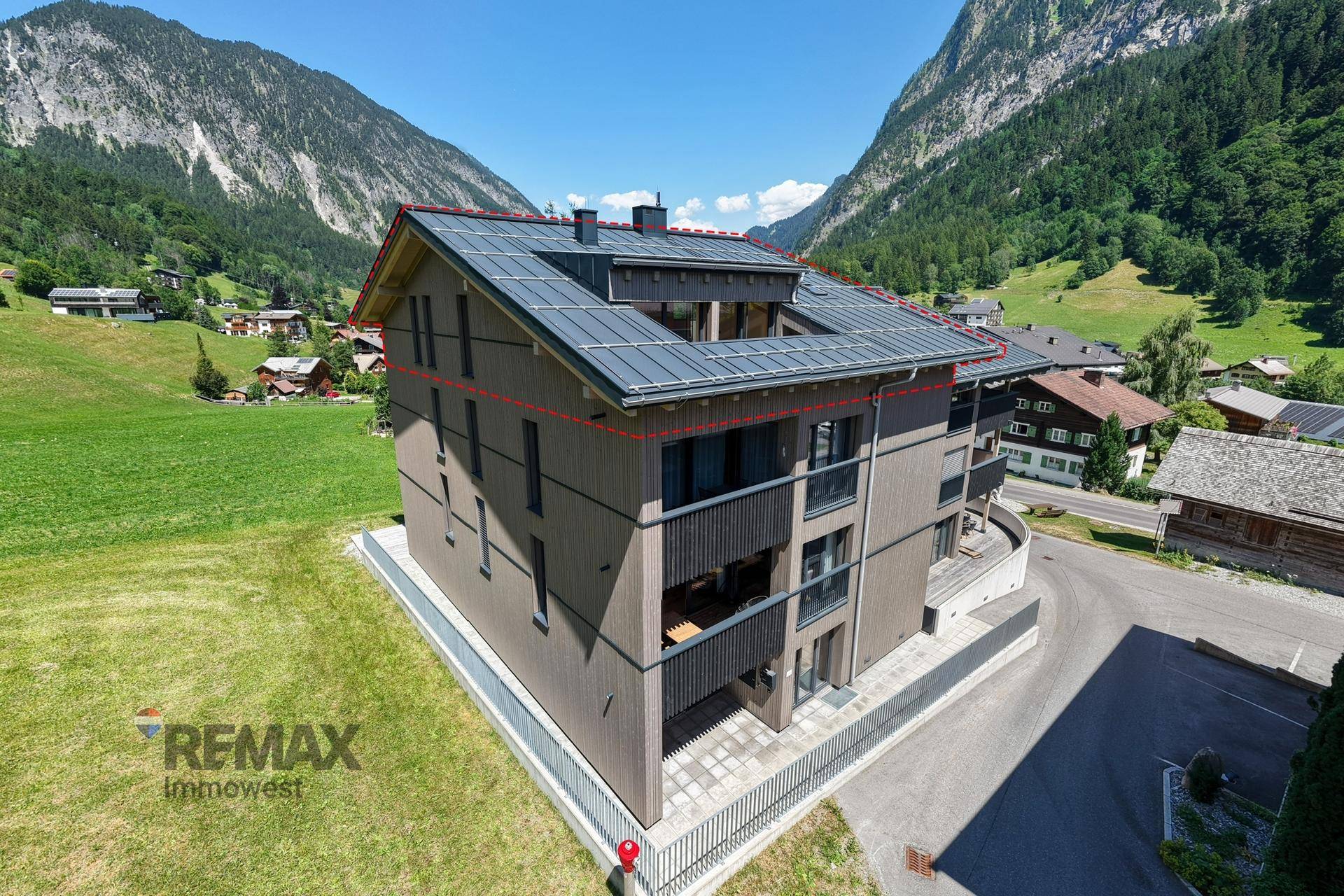 Luftaufnahme eines modernen Gebäudes mit Solaranlage und Bergblick in grüner Umgebung.