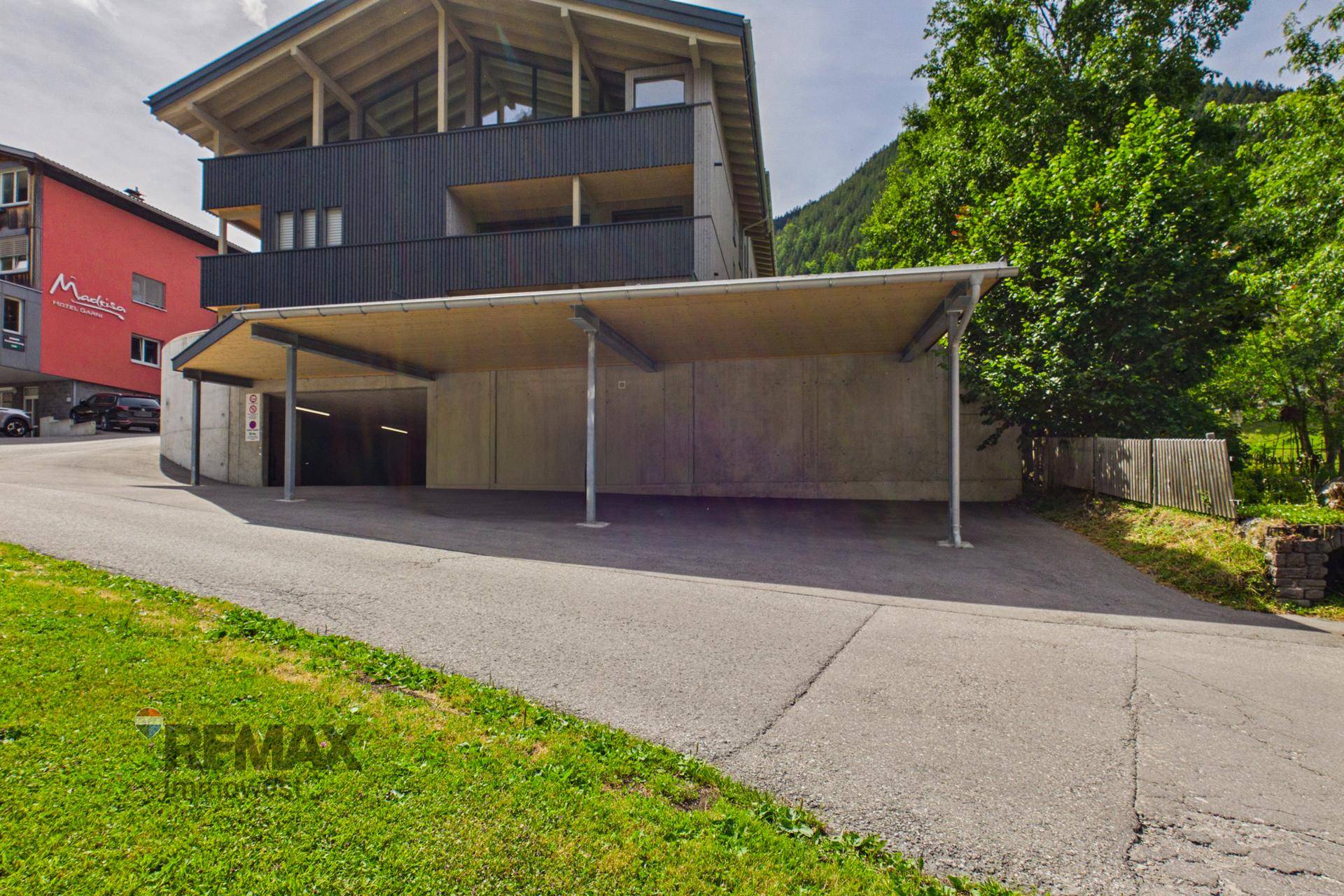 Zufahrt zu einem modernen Gebäude mit Carport und Tiefgarageneinfahrt.