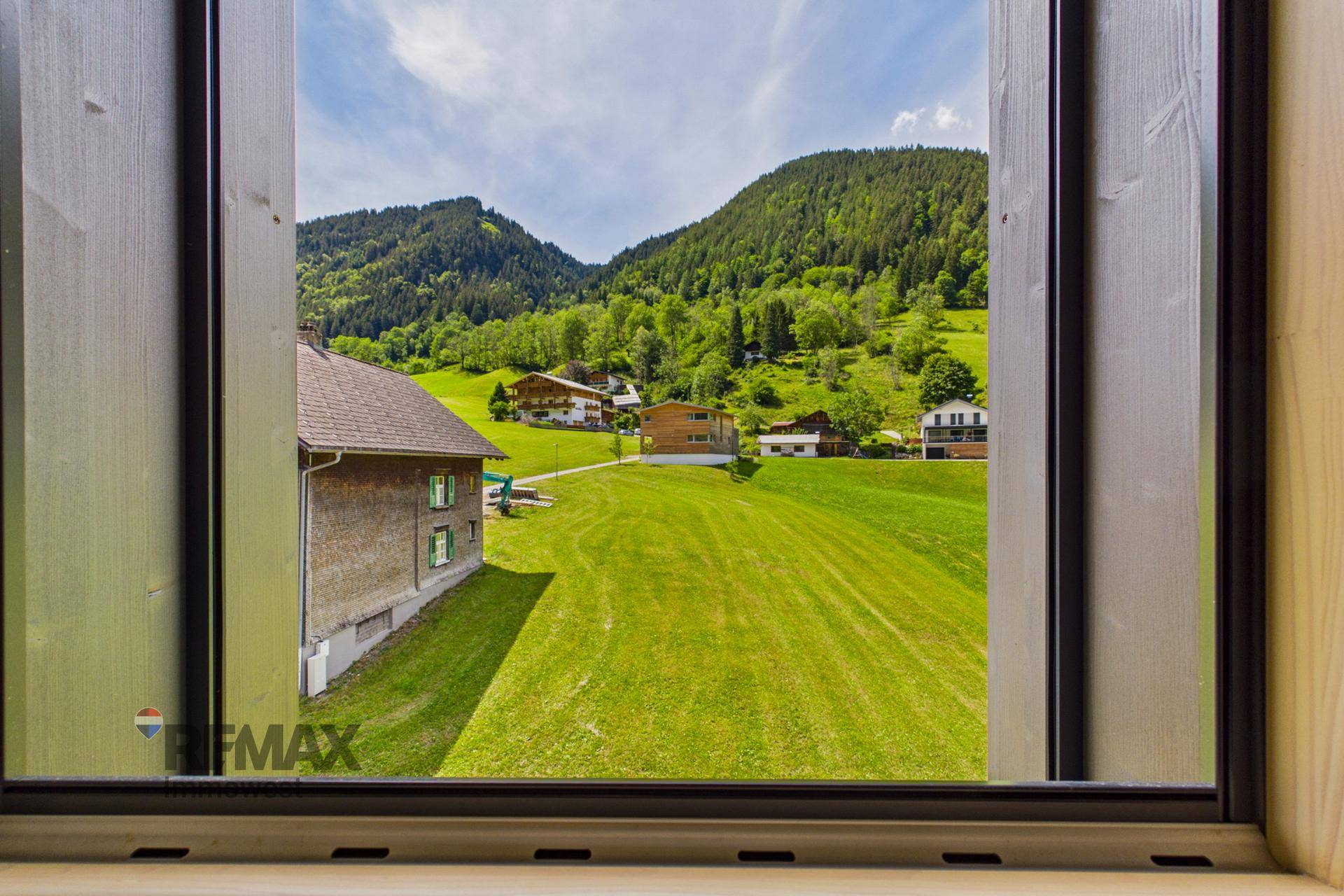 Malerischer Ausblick aus dem Fenster auf grüne Wiesen und Berge.