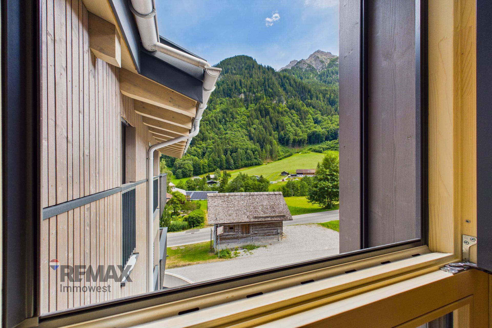 Fensterblick auf ein traditionelles Holzhaus und die umliegende Berglandschaft.