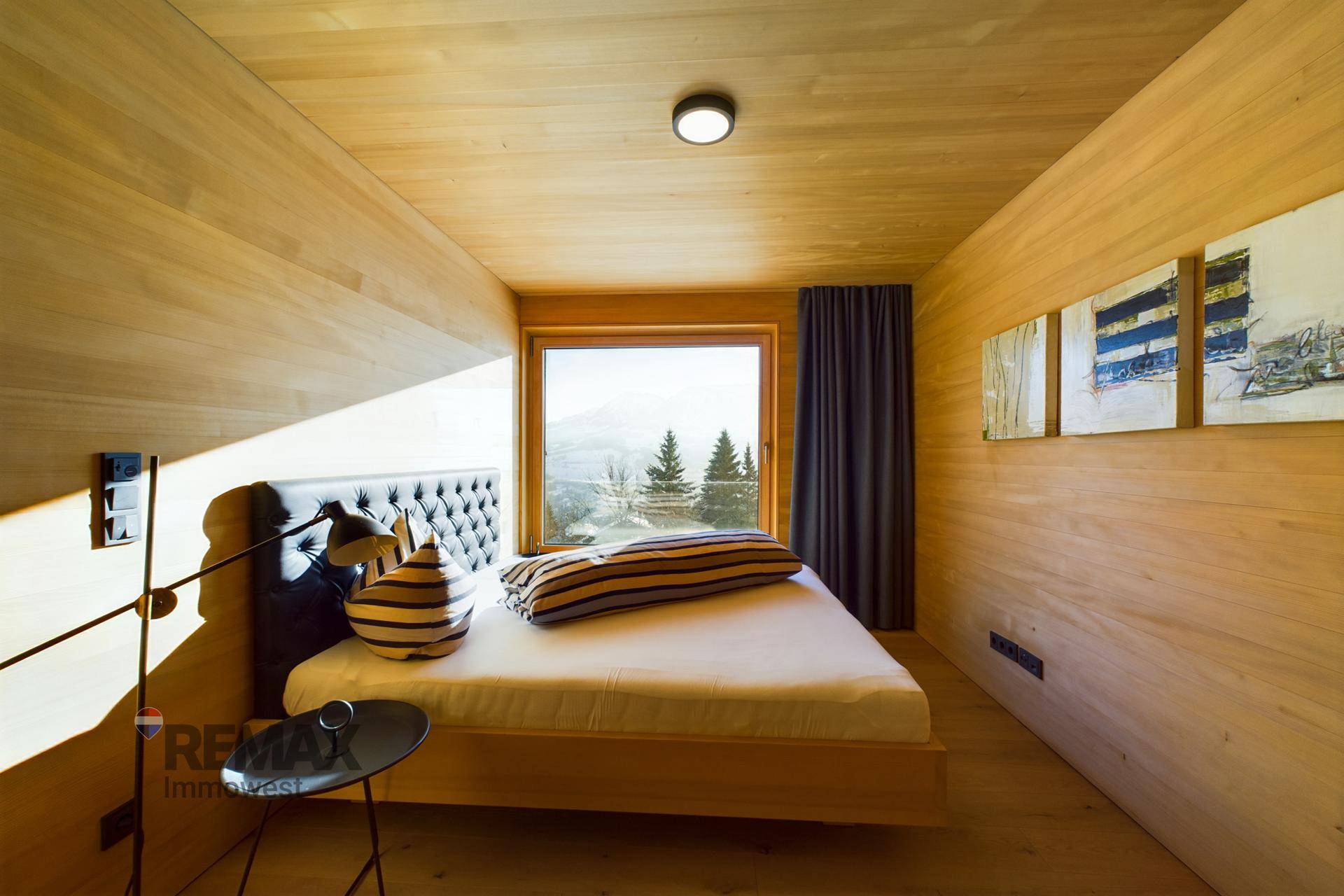 Schlafzimmer mit Holzwänden, bequemen Bett und Fenster mit Blick auf die Natur.