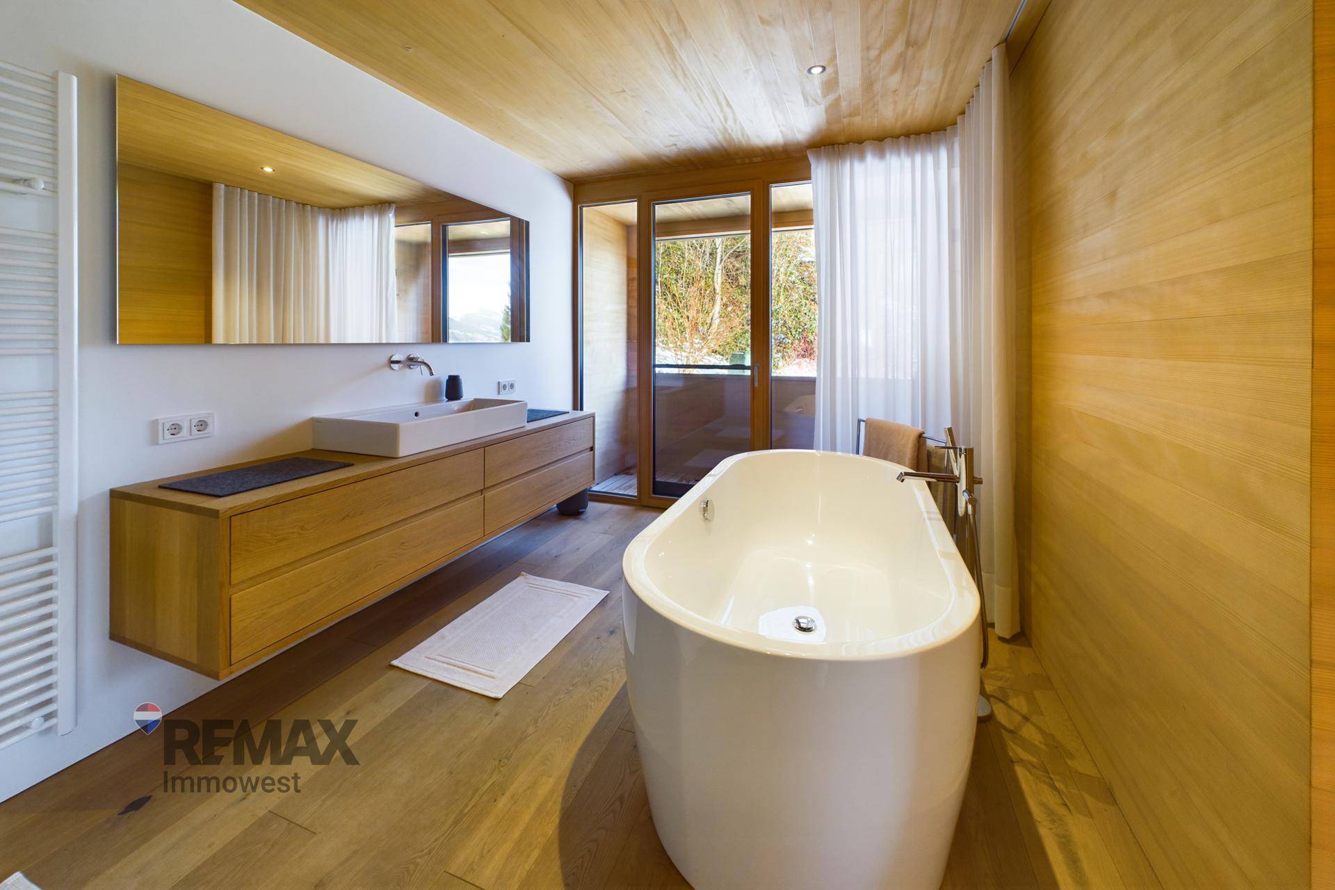 Modernes Badezimmer mit freistehender Badewanne, Holzwaschtisch und Zugang nach draußen.