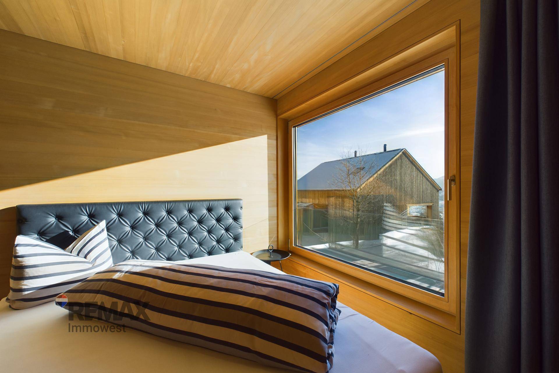 Helles Schlafzimmer mit Holzwänden und großem Fenster mit Blick auf die Nachbarschaft.