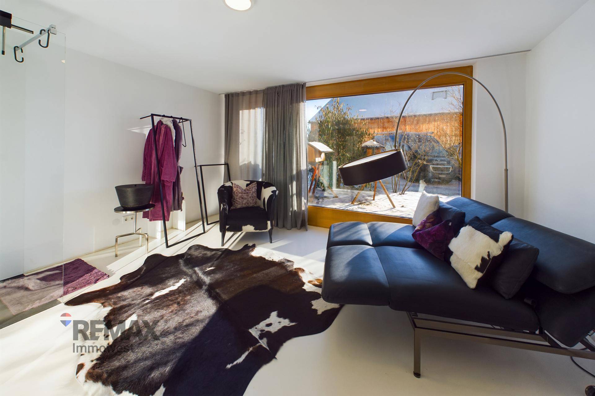 Heller Raum mit Sofa, Kleiderstange und großem Fenster mit Blick in den Garten.