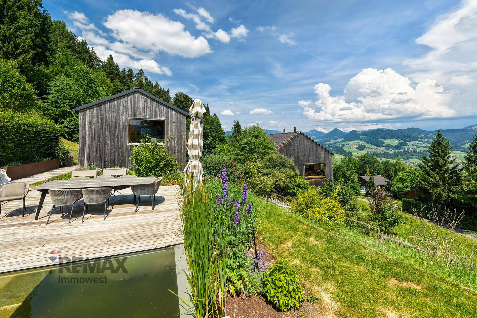 Elegante Holzterrasse mit Esstisch und Pflanzen, bietet einen weiten Blick auf die umliegende Berglandschaft.