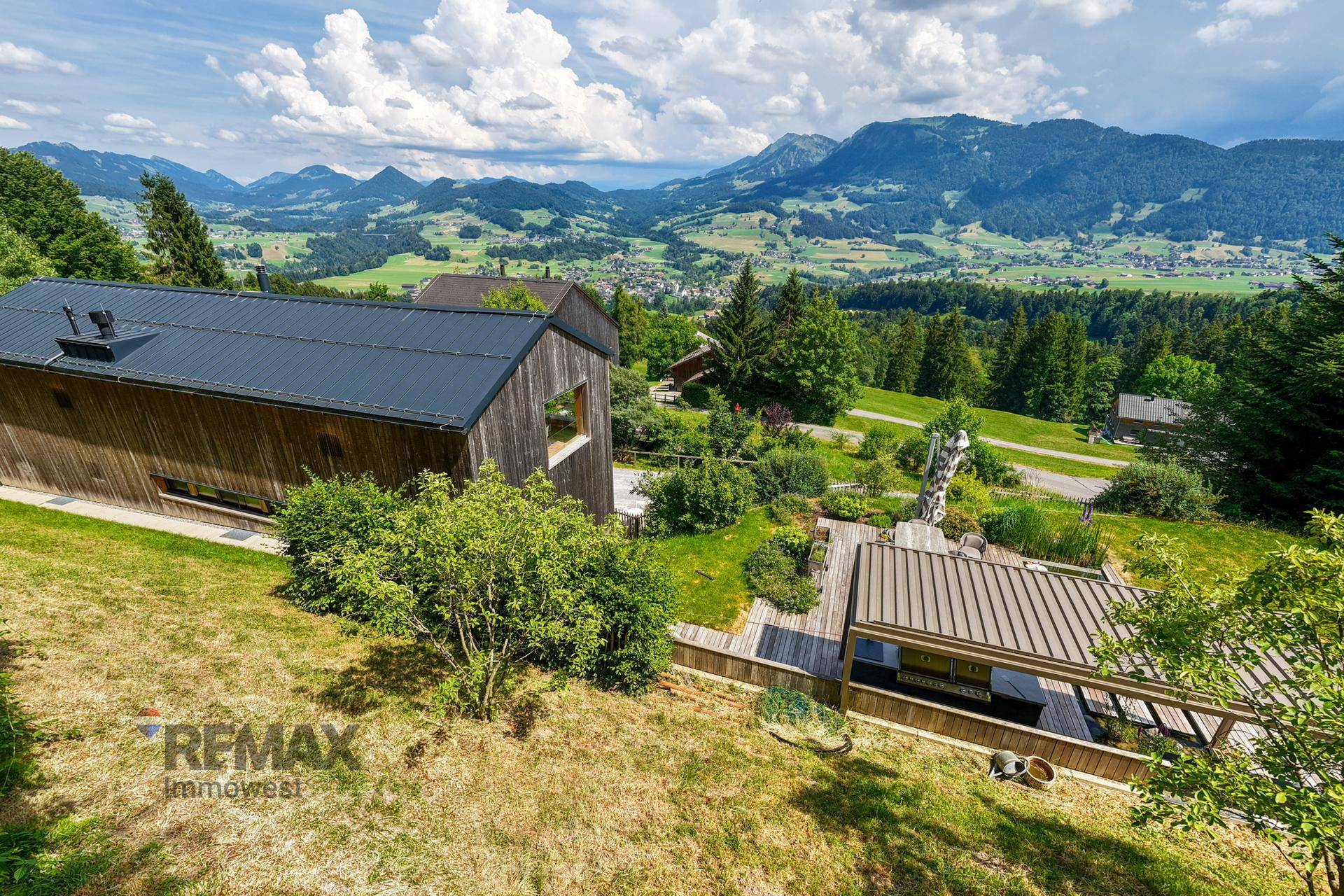 Panoramablick auf moderne Holzhäuser in alpiner Landschaft mit weitem Bergblick unter blauem Himmel.