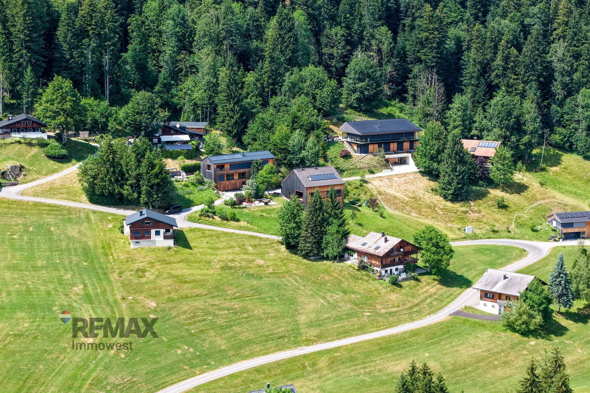 Luftaufnahme einer Siedlung mit mehreren modernen Holzhäusern, eingebettet in eine grüne Hügellandschaft.