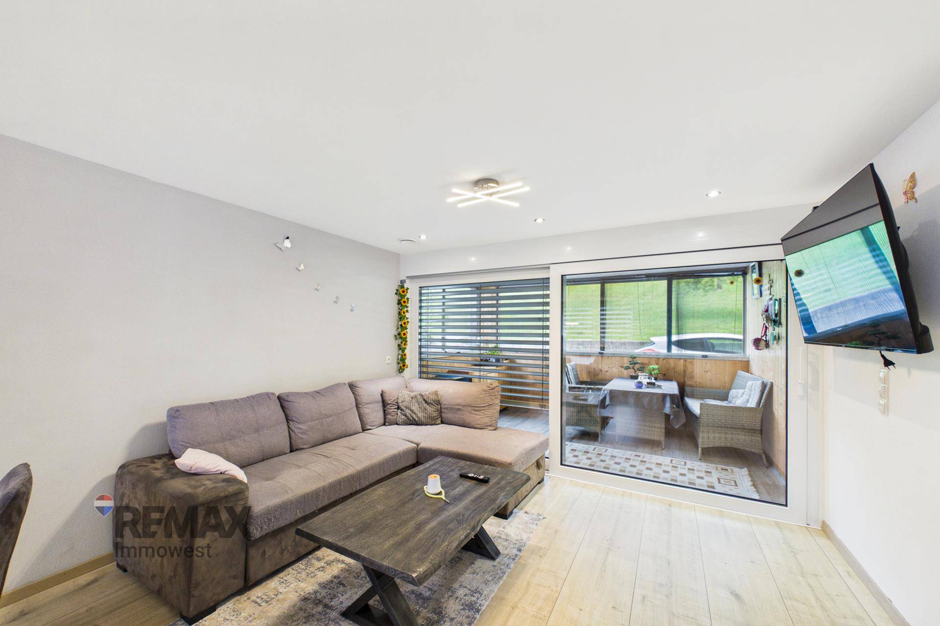 Gemütliches Wohnzimmer mit Ecksofa, Couchtisch und großen Fenstern zum verglasten Balkon.