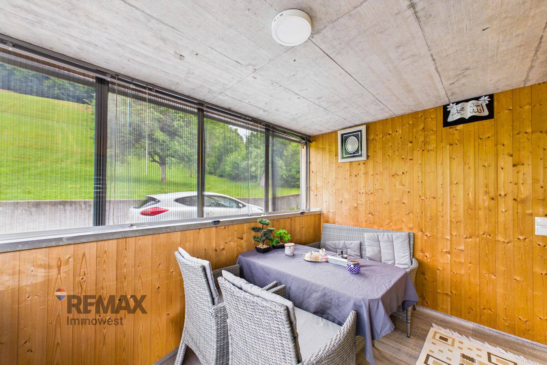Gemütliche Loggia mit Holzwänden, Esstisch und Blick auf die umliegenden grünen Hügel.