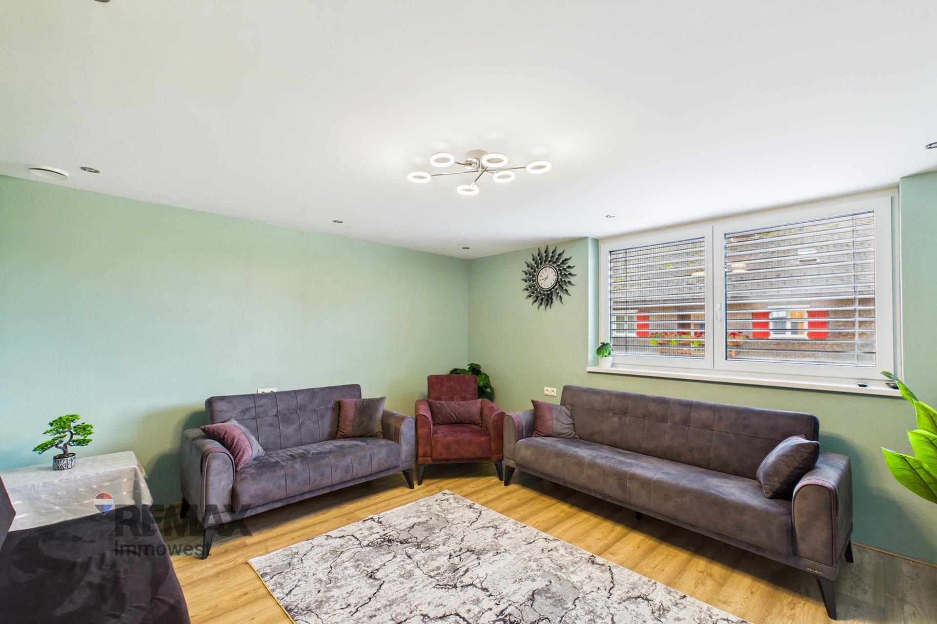 Geräumiges Wohnzimmer mit bequemen Sofas, Teppich und Fenster mit Jalousien.