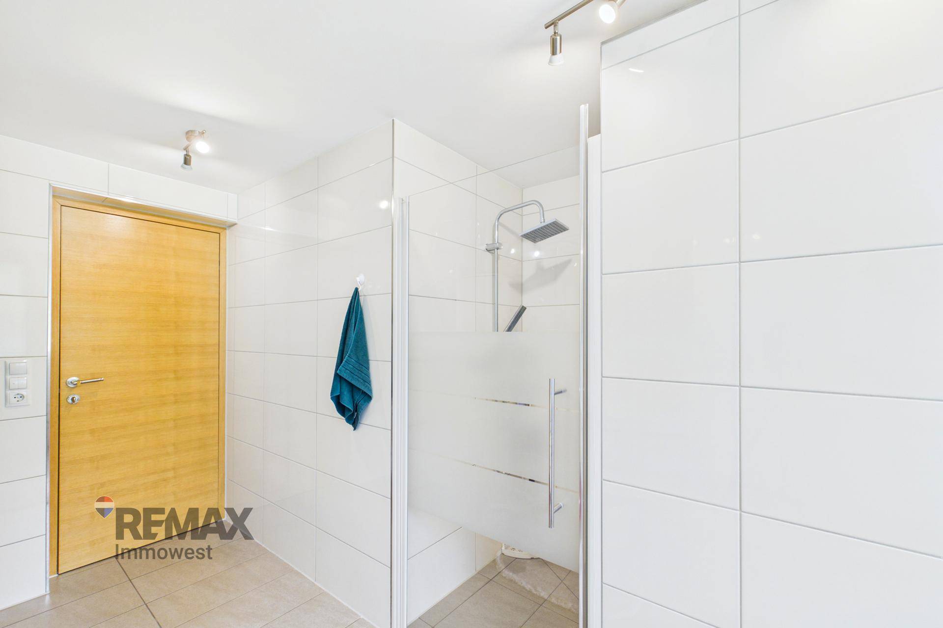 Badezimmer mit weiß gefliestem Duschbereich und Holztür.