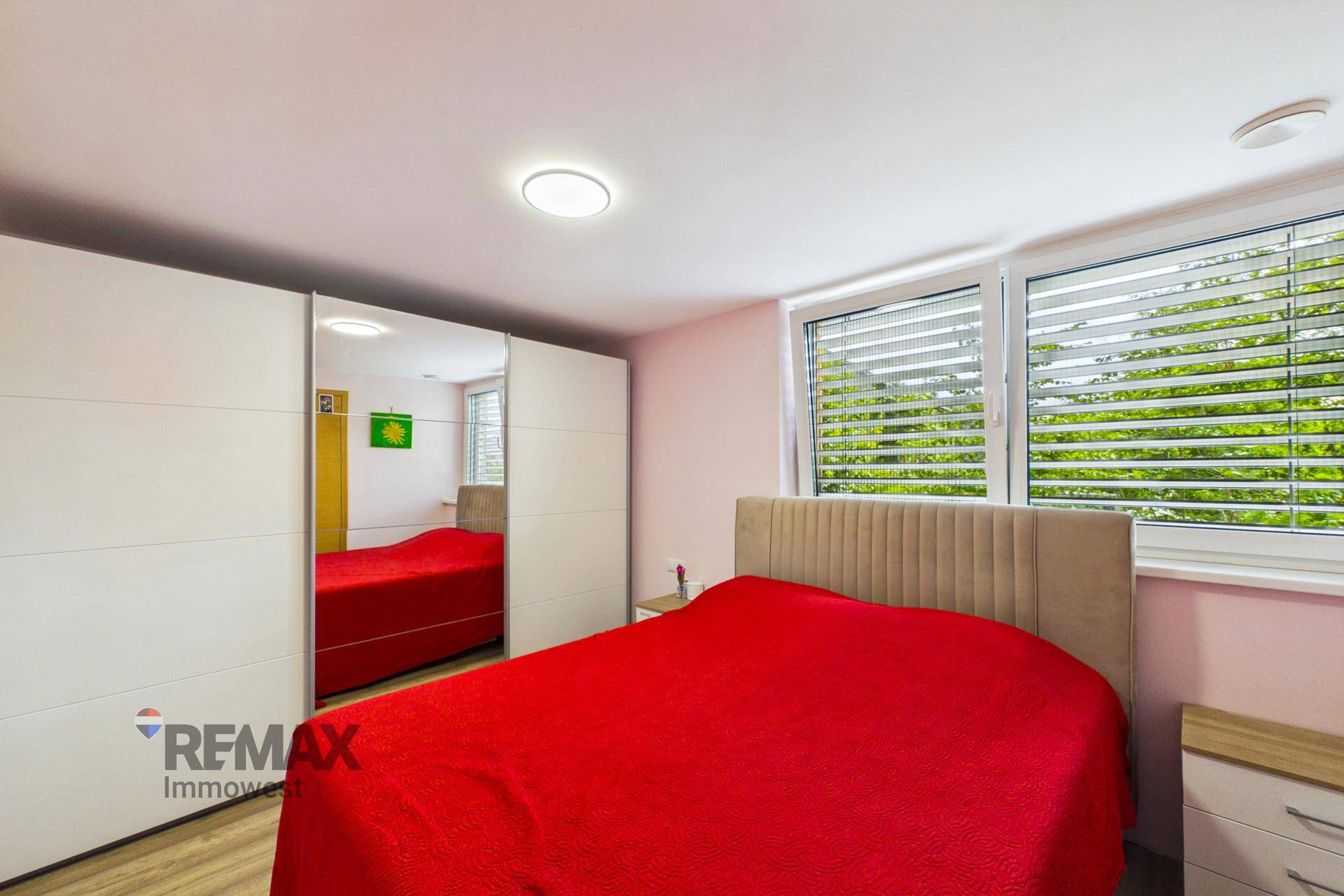 Schlafzimmer mit rotem Bett, Spiegelschrank und Blick ins Grüne.