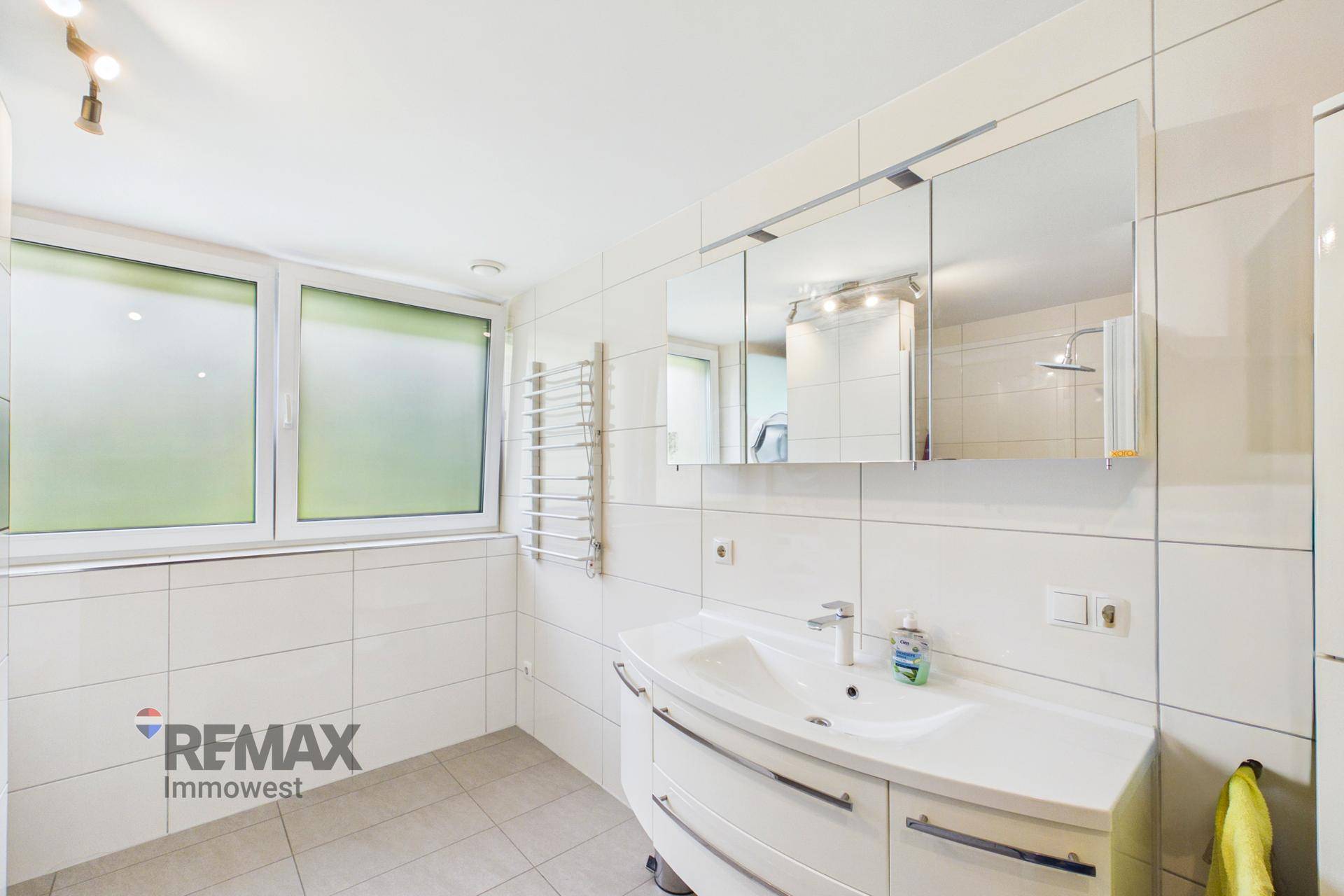 Modernes Badezimmer mit weißen Fliesen, Einzelwaschbecken und Fenster.