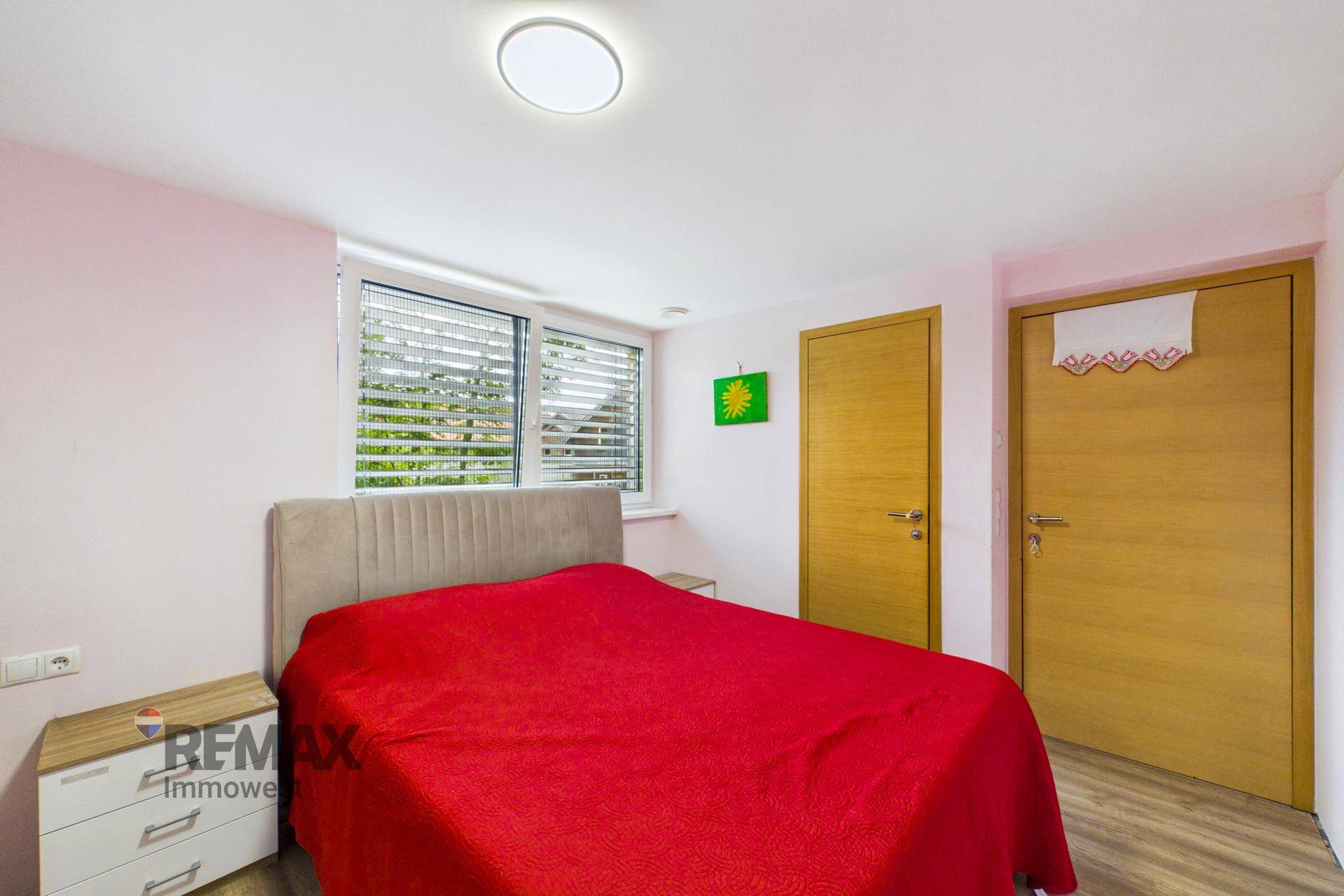 Schlafzimmer mit rotem Bett, Holzboden und zwei Holztüren.