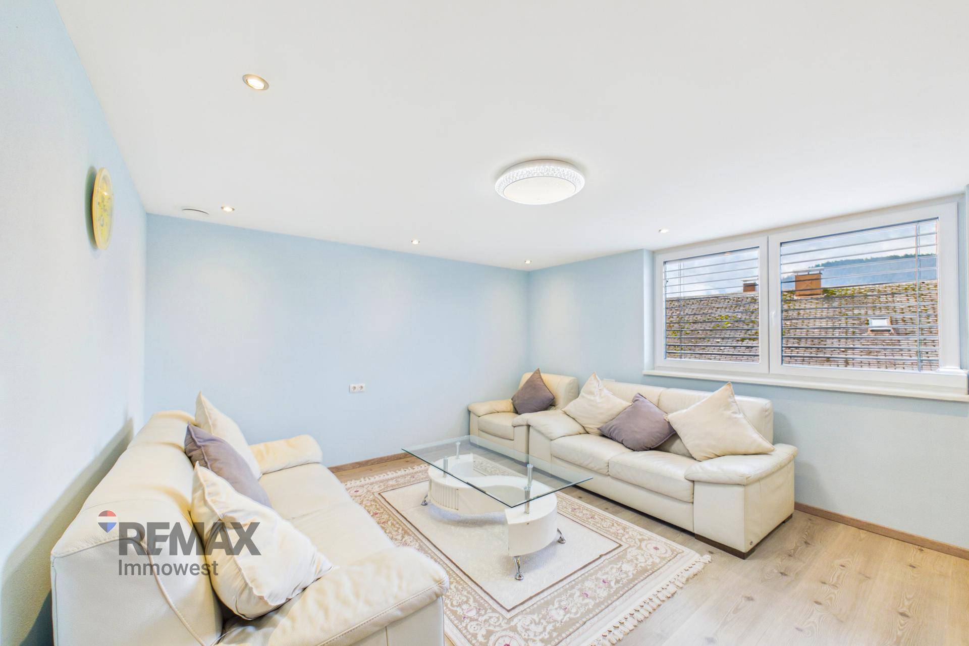 Helles Wohnzimmer mit blauen Wänden, weißen Sofas und Holzboden.
