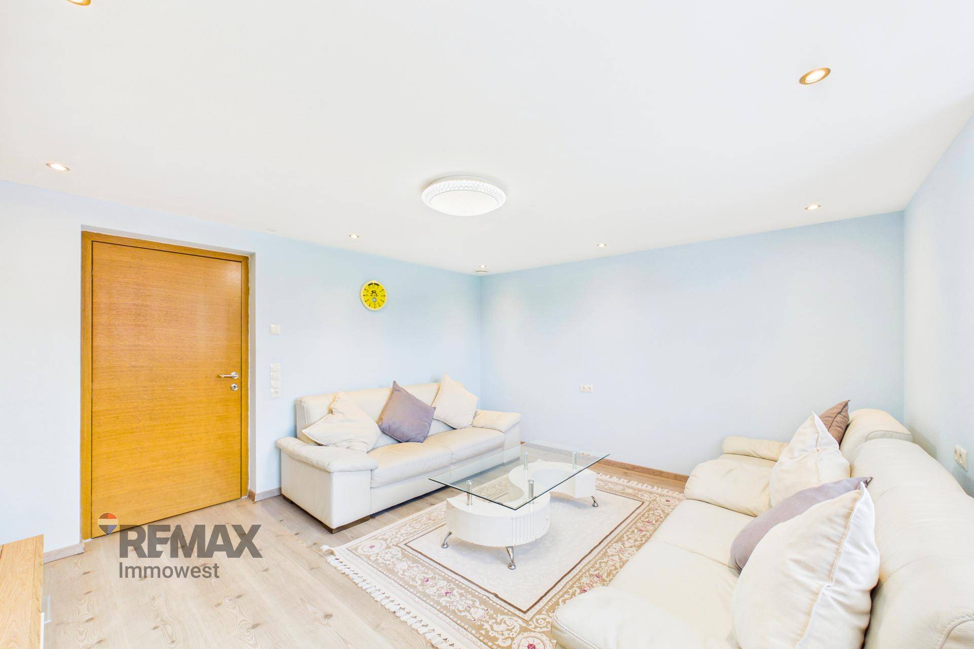Wohnzimmer mit blauen Wänden, weißen Sofas und Holztür.