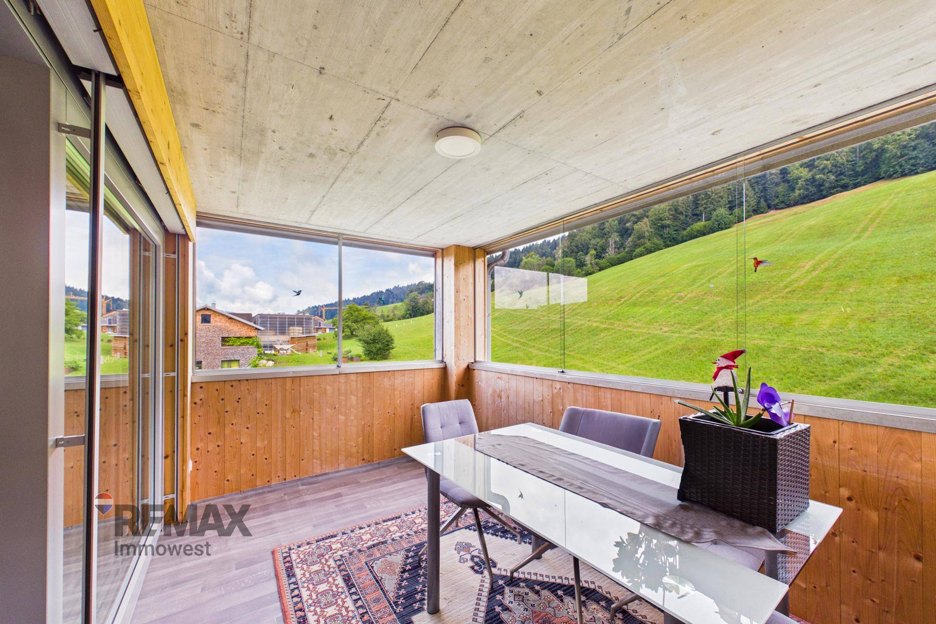 Verglaste Loggia mit Esstisch und Stühlen, umgeben von grüner Landschaft.