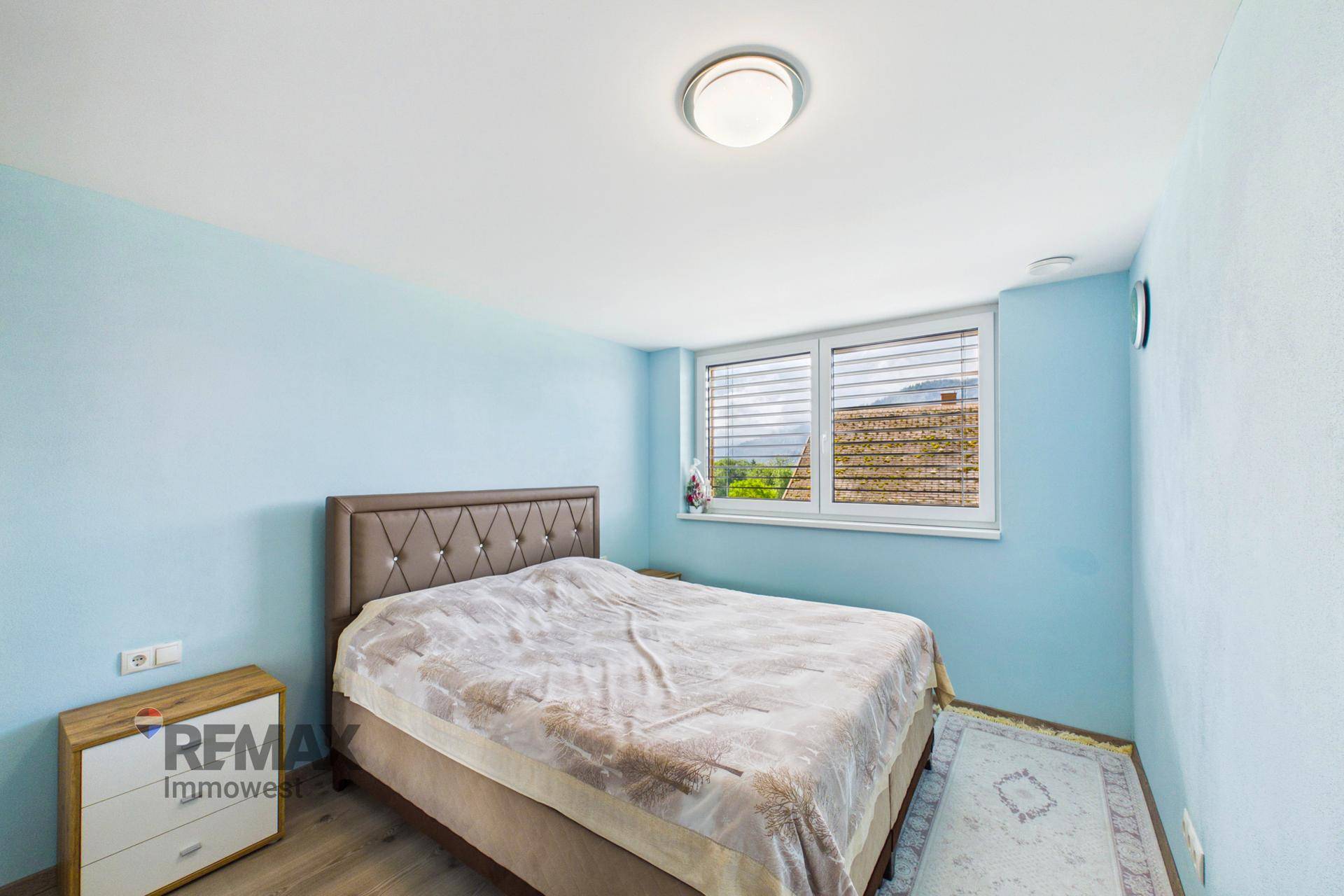 Schlafzimmer mit blauen Wänden, Doppelbett und Fensterblick.