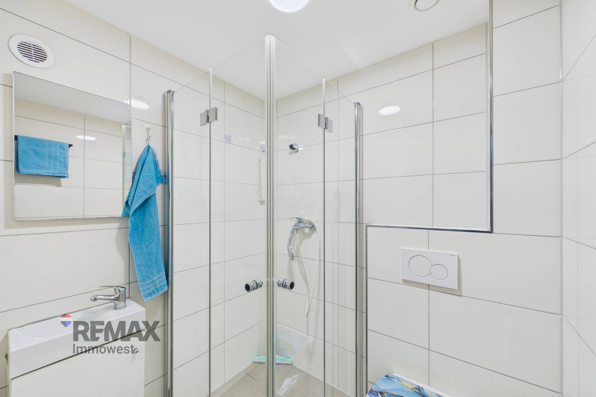 Badezimmer mit weiß gefliestem Duschbereich und Wand-WC.