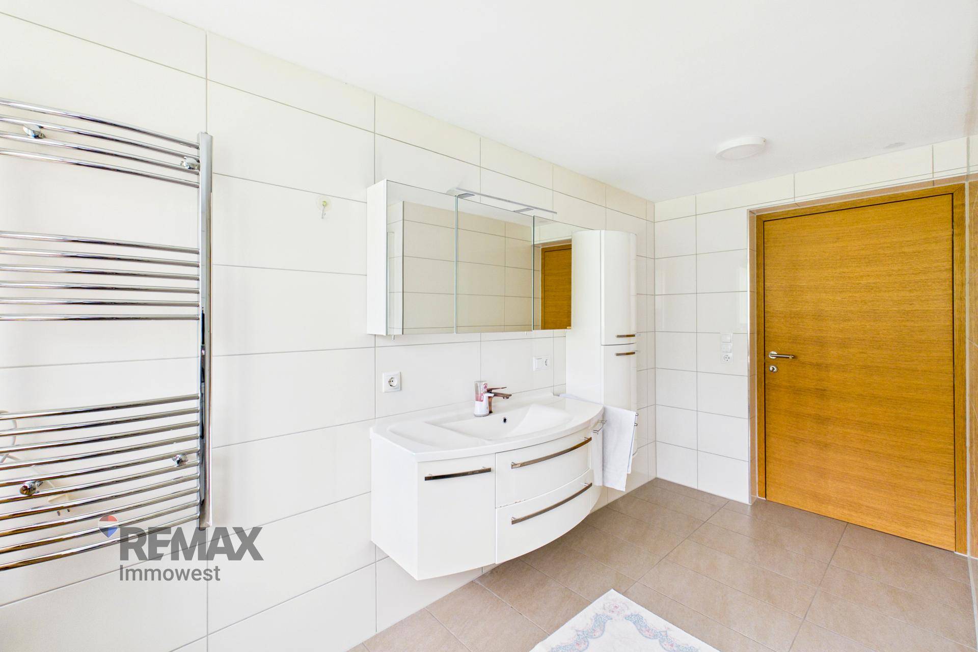 Modernes Badezimmer mit weißen Fliesen, Einzelwaschbecken und beheiztem Handtuchhalter.