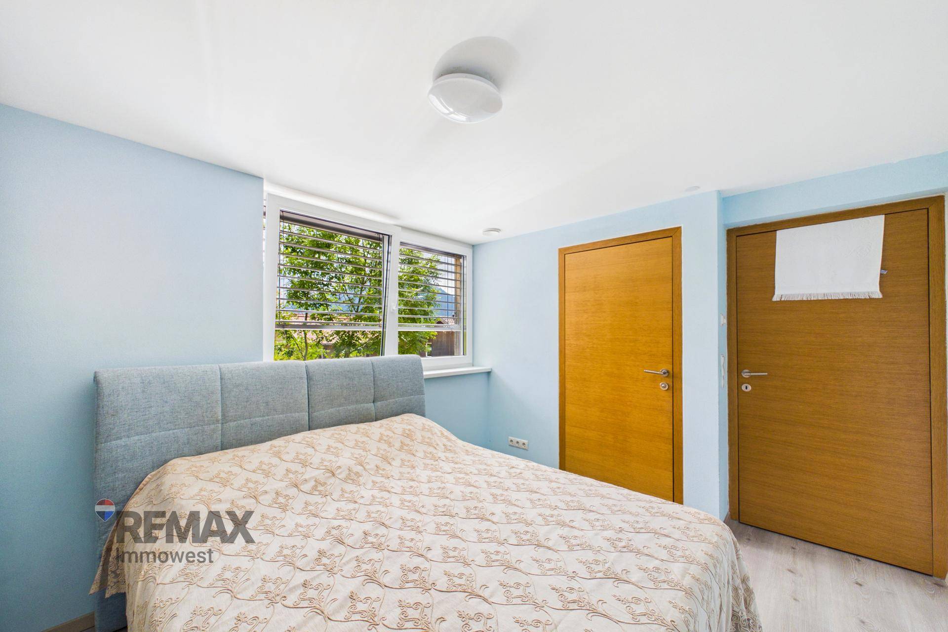 Schlafzimmer mit blauen Wänden, Doppelbett und zwei Holztüren.