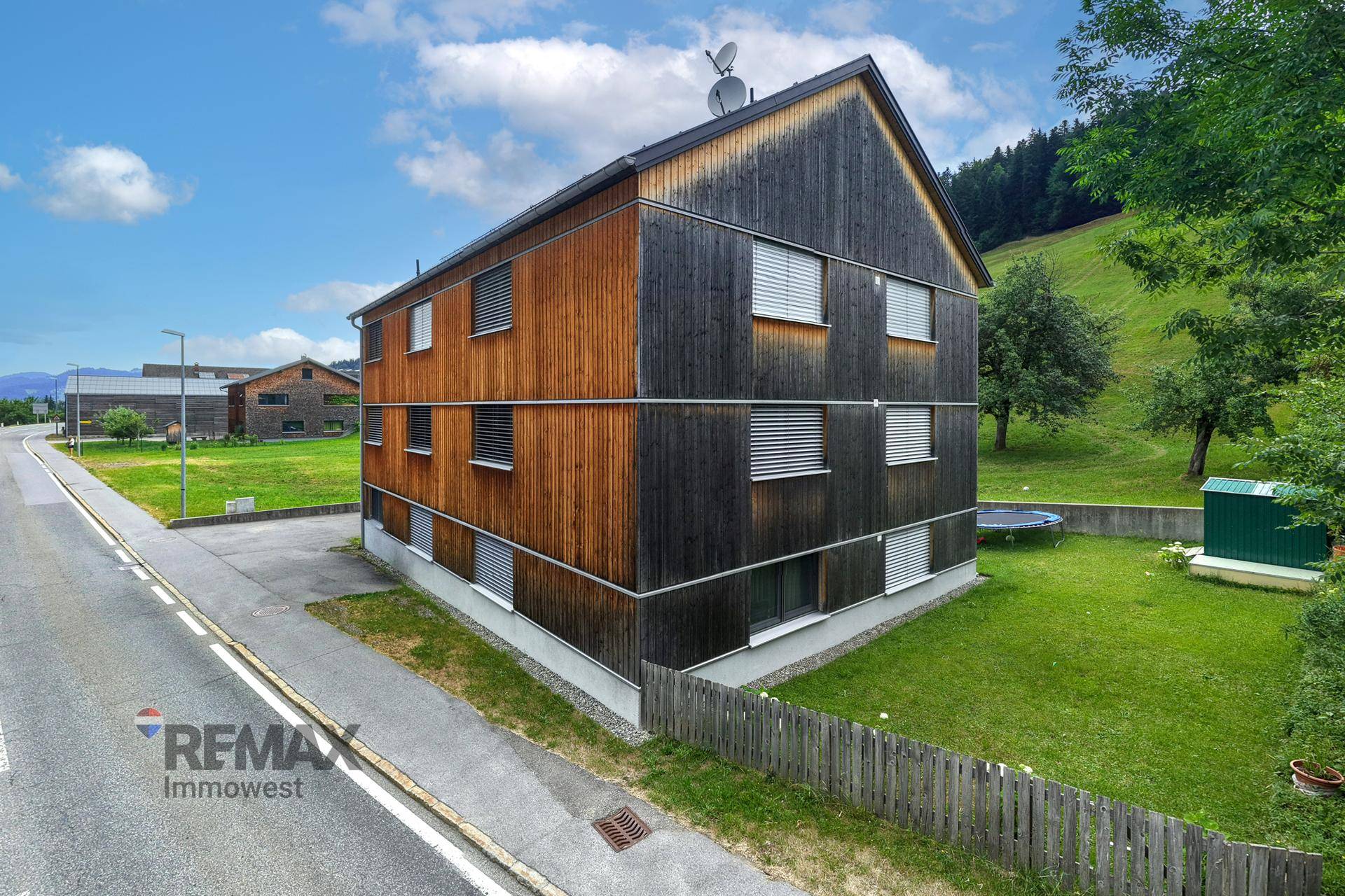 Modernes Holzhaus mit Satteldach und grüner Umgebung.