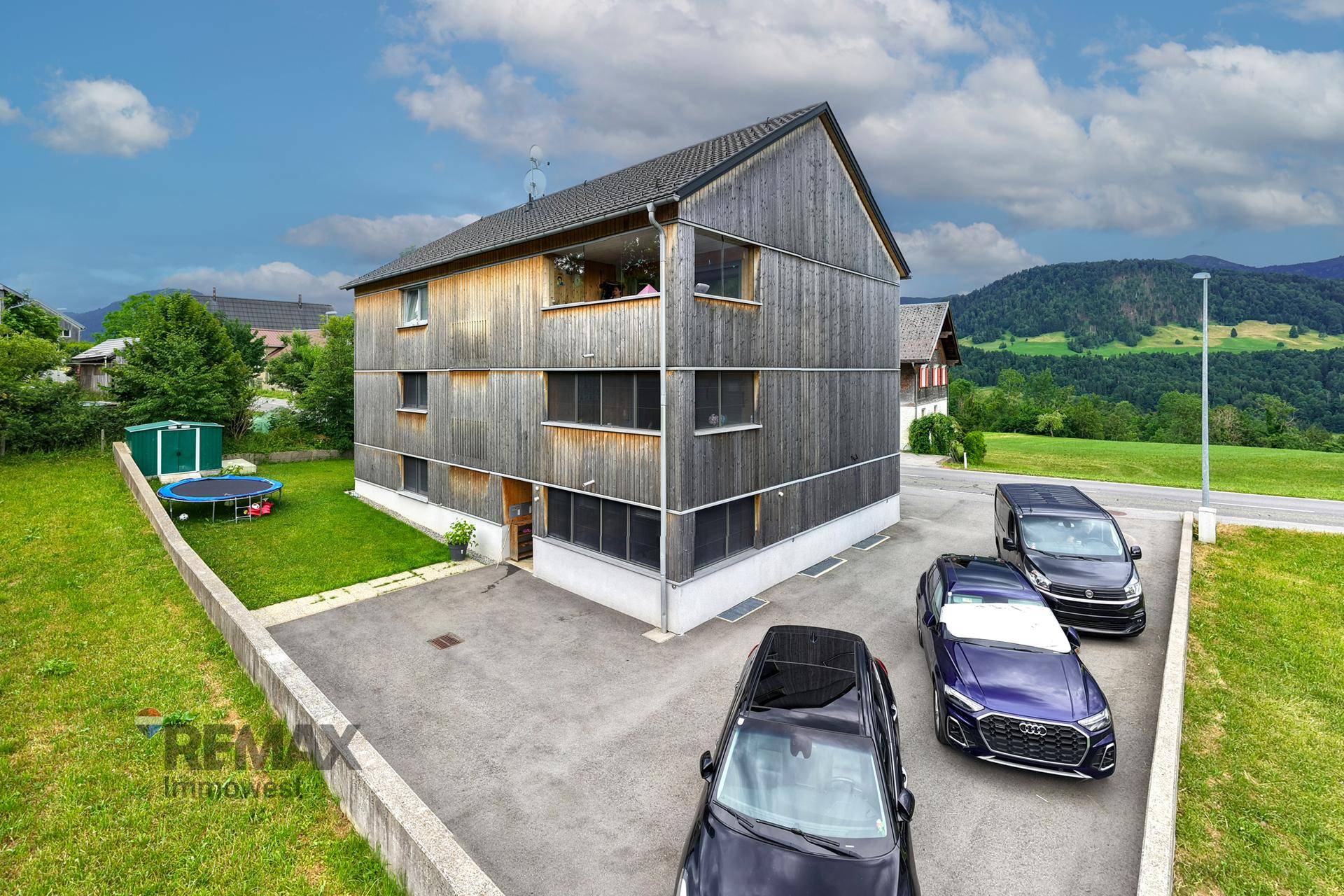 Modernes Holzhaus mit Parkplätzen und grüner Umgebung.