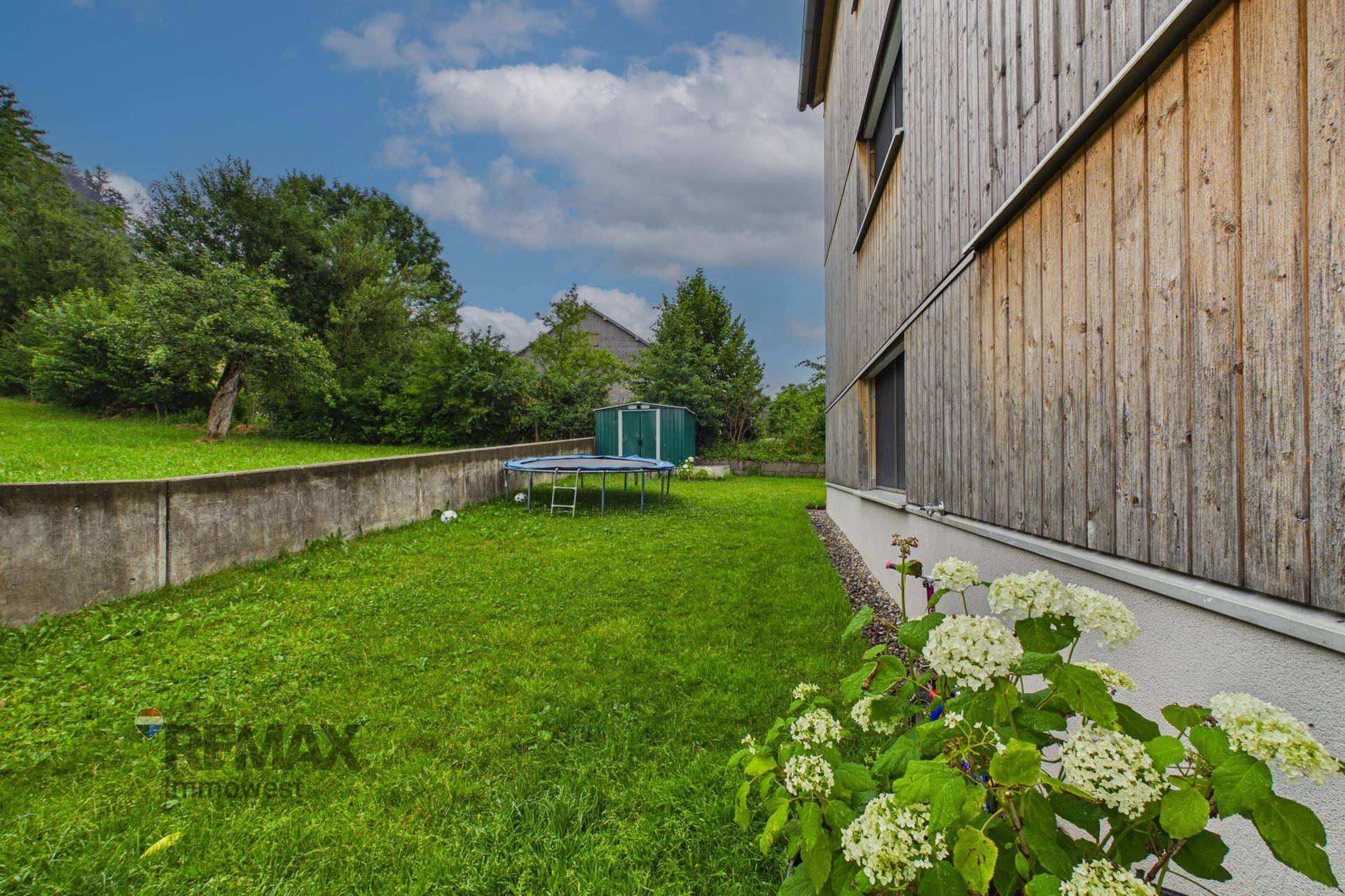 Grüner Gartenbereich mit Rasen, Blumen und Trampolin neben dem Gebäude.