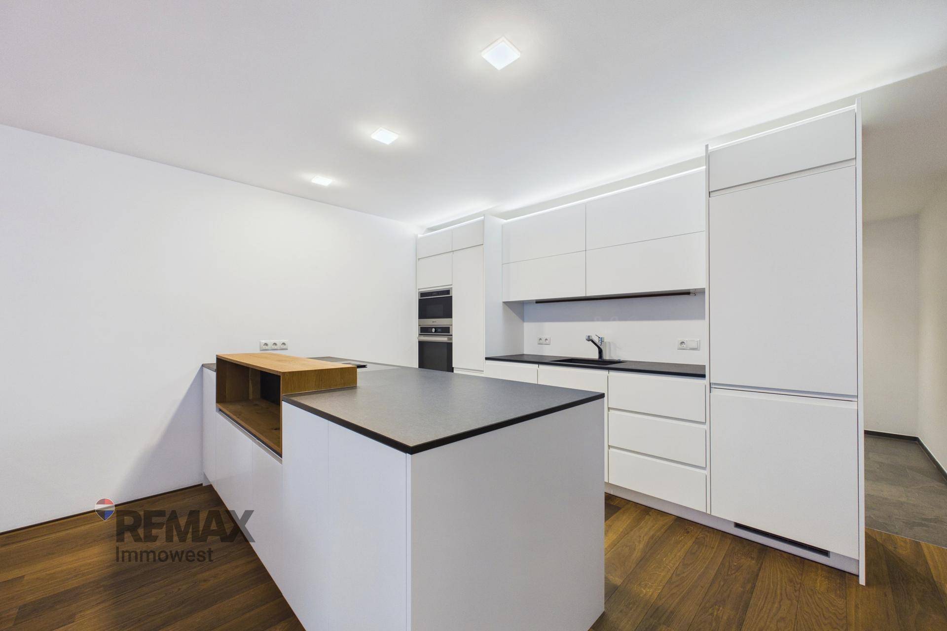 Elegante, moderne Küche mit weißen Schränken, dunkler Arbeitsplatte und integrierten Geräten.