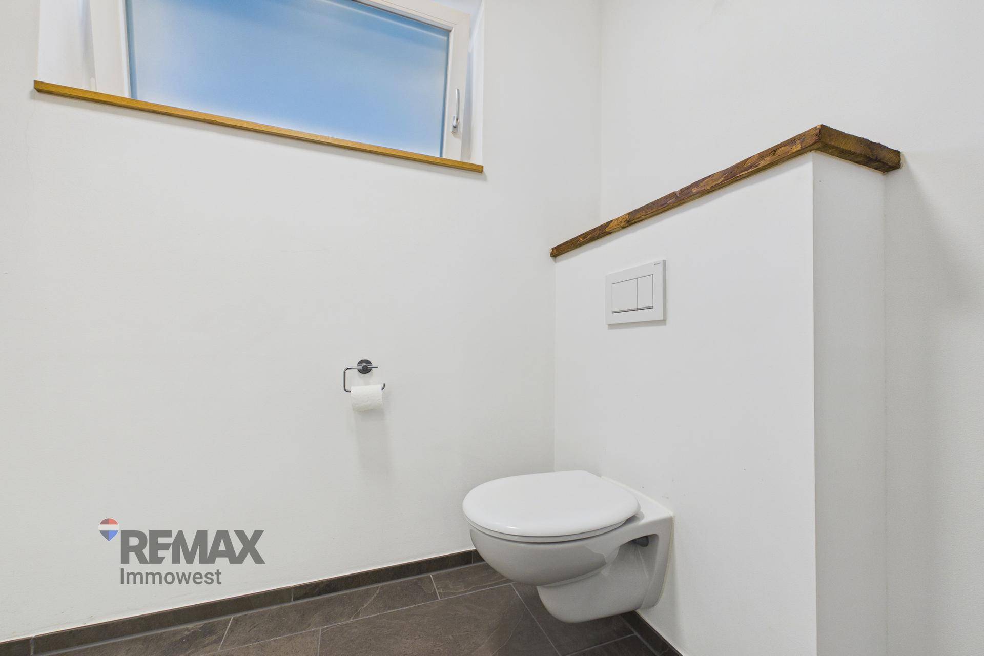 Helles WC mit wandhängender Toilette, Holzablage und kleinem Fenster für natürliche Belüftung.
