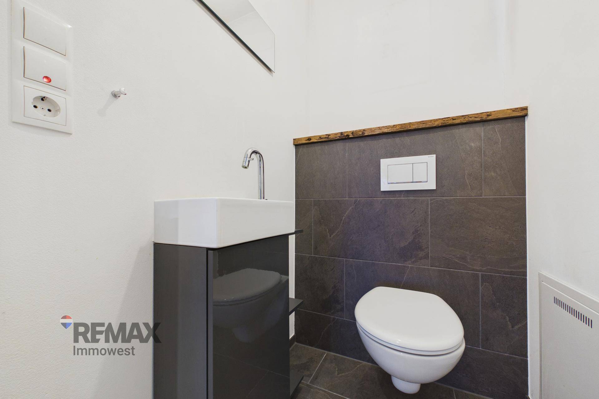 Stilvolles Gäste-WC mit dunklen Wandfliesen, modernem Waschtisch und wandhängender Toilette.