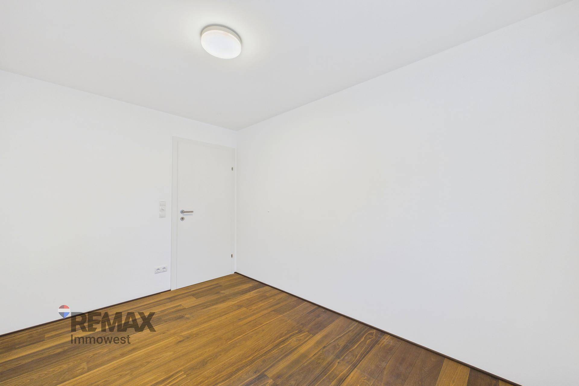 Geräumiges, unmöbliertes Zimmer mit Holzboden und weißer Tür, bereit zur individuellen Gestaltung.