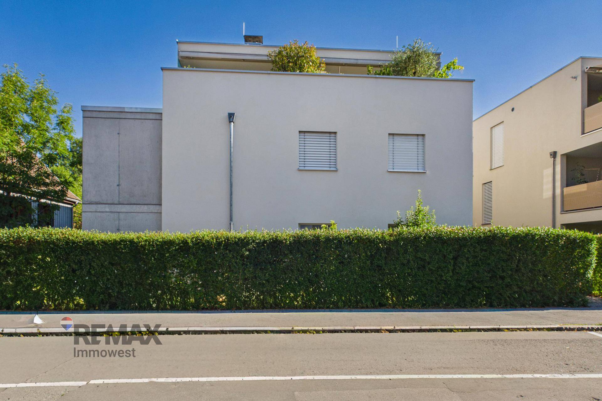Ansicht der modernen Gebäudefassade von der Straße, mit gepflegter Hecke im Vordergrund.