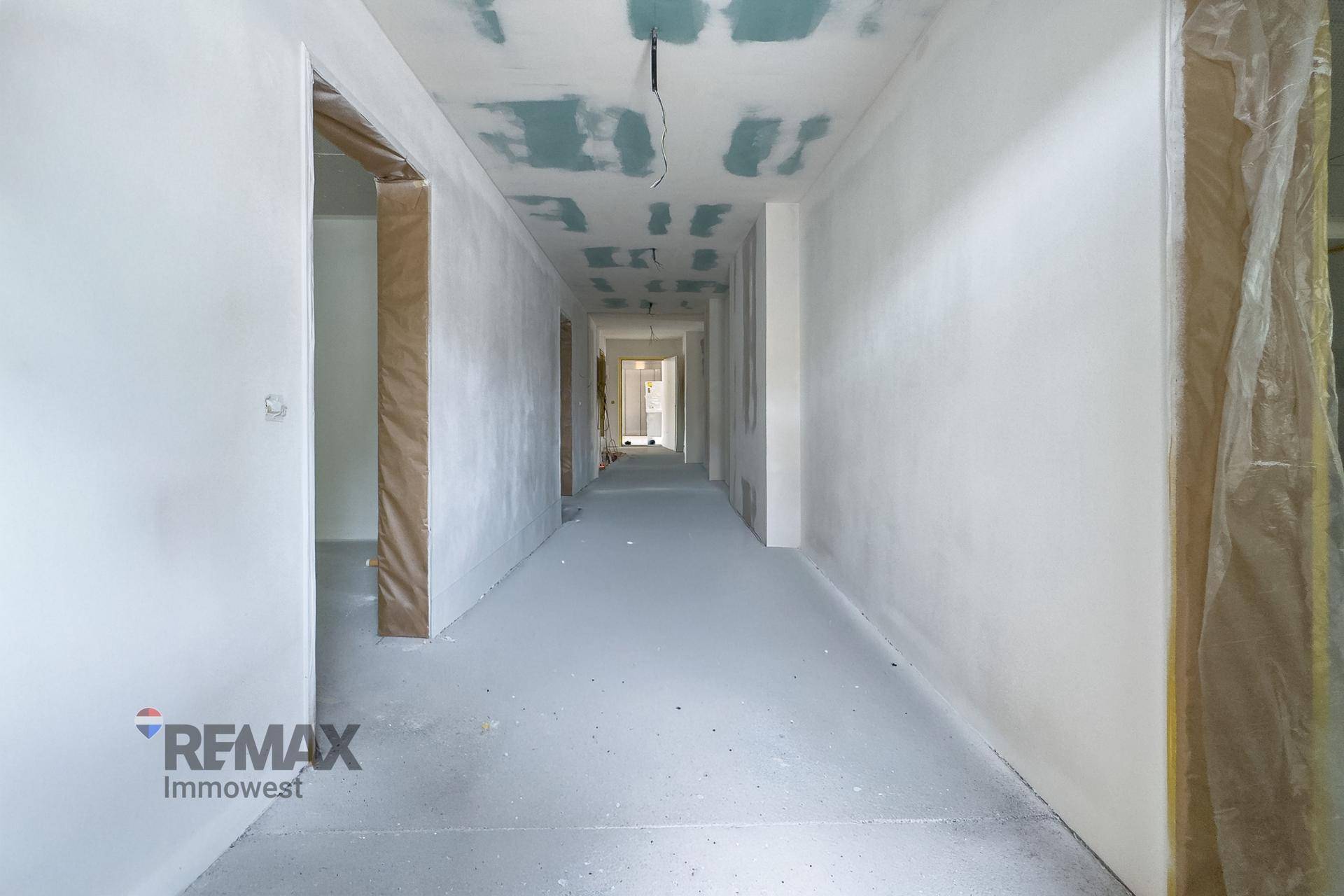 Langer Flur im Rohbauzustand mit Betonboden und unfertiger Decke, bereit für den Ausbau.