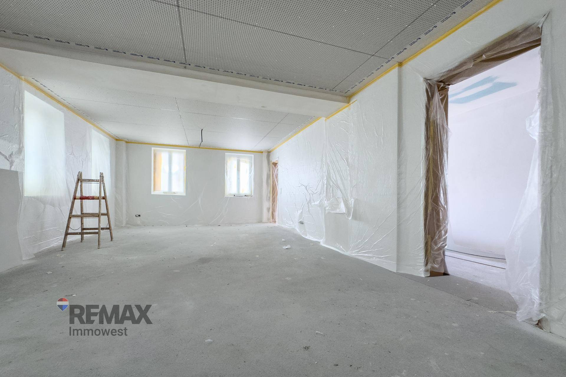 Rohbau-Raum mit abgedeckten Wänden, Betonboden und einer Leiter, bereit für den Ausbau.
