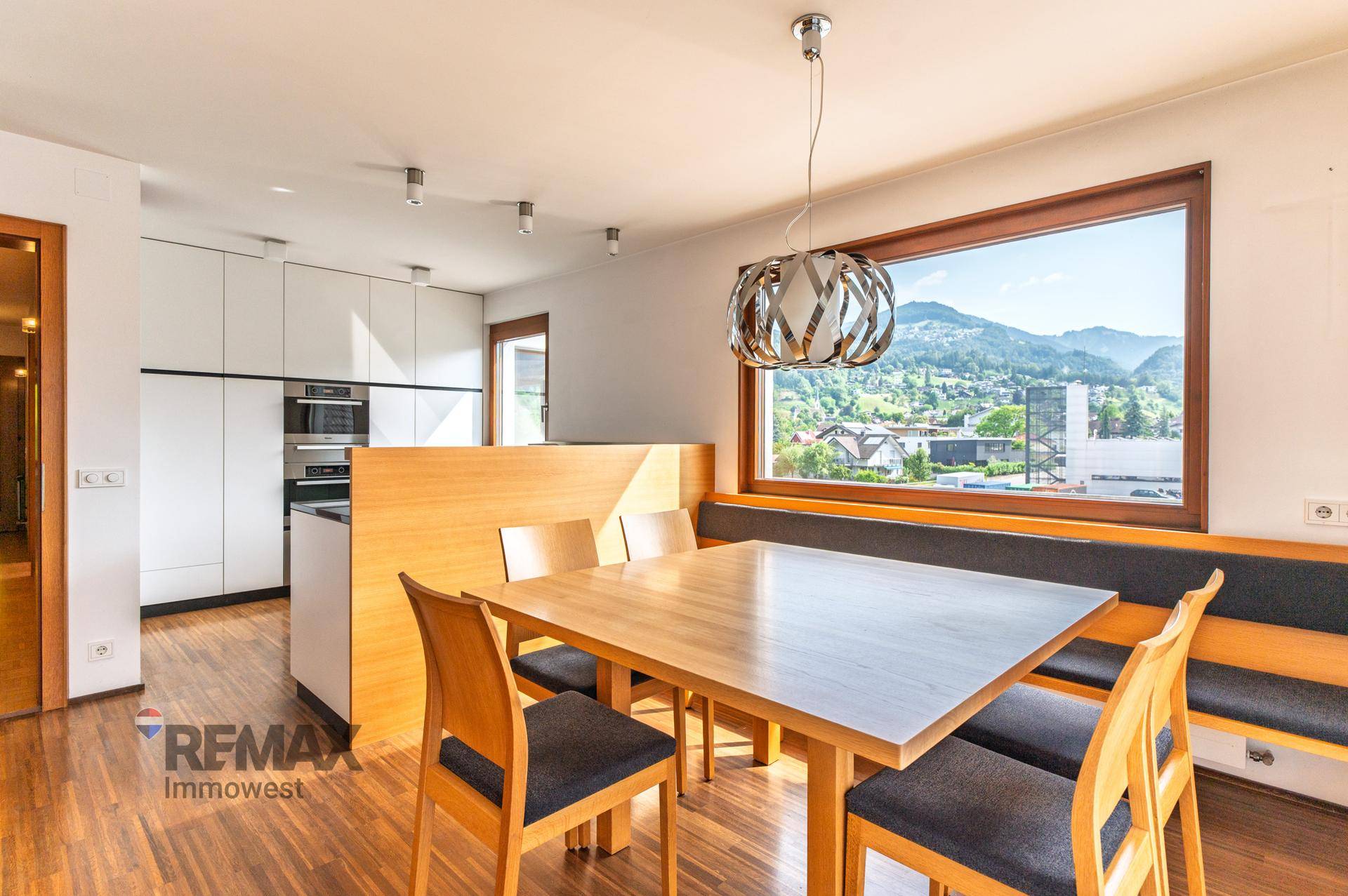 Moderne Küche mit Essbereich, Holzboden und großem Fenster mit Bergblick.