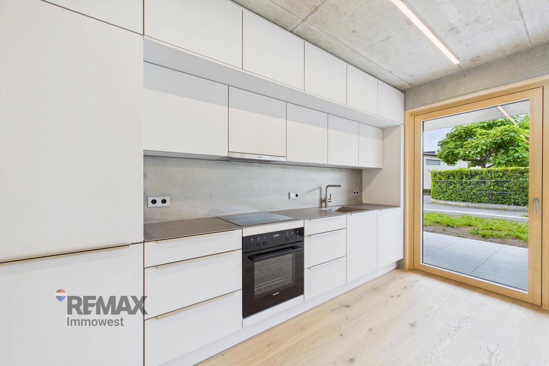 Moderne Einbauküche mit weißen Fronten, Induktionskochfeld und Zugang zum Außenbereich.
