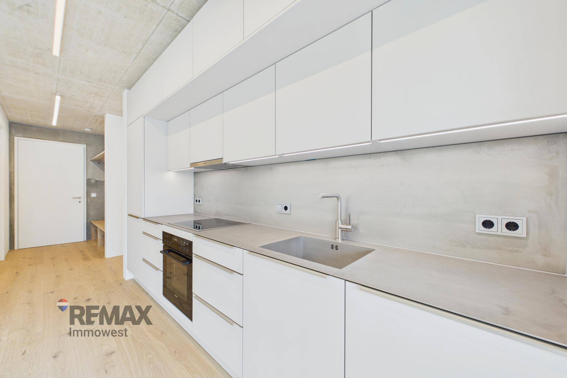 Zeitgemäße Küche mit weißen Schränken, integrierten Geräten und Beton-Decke.