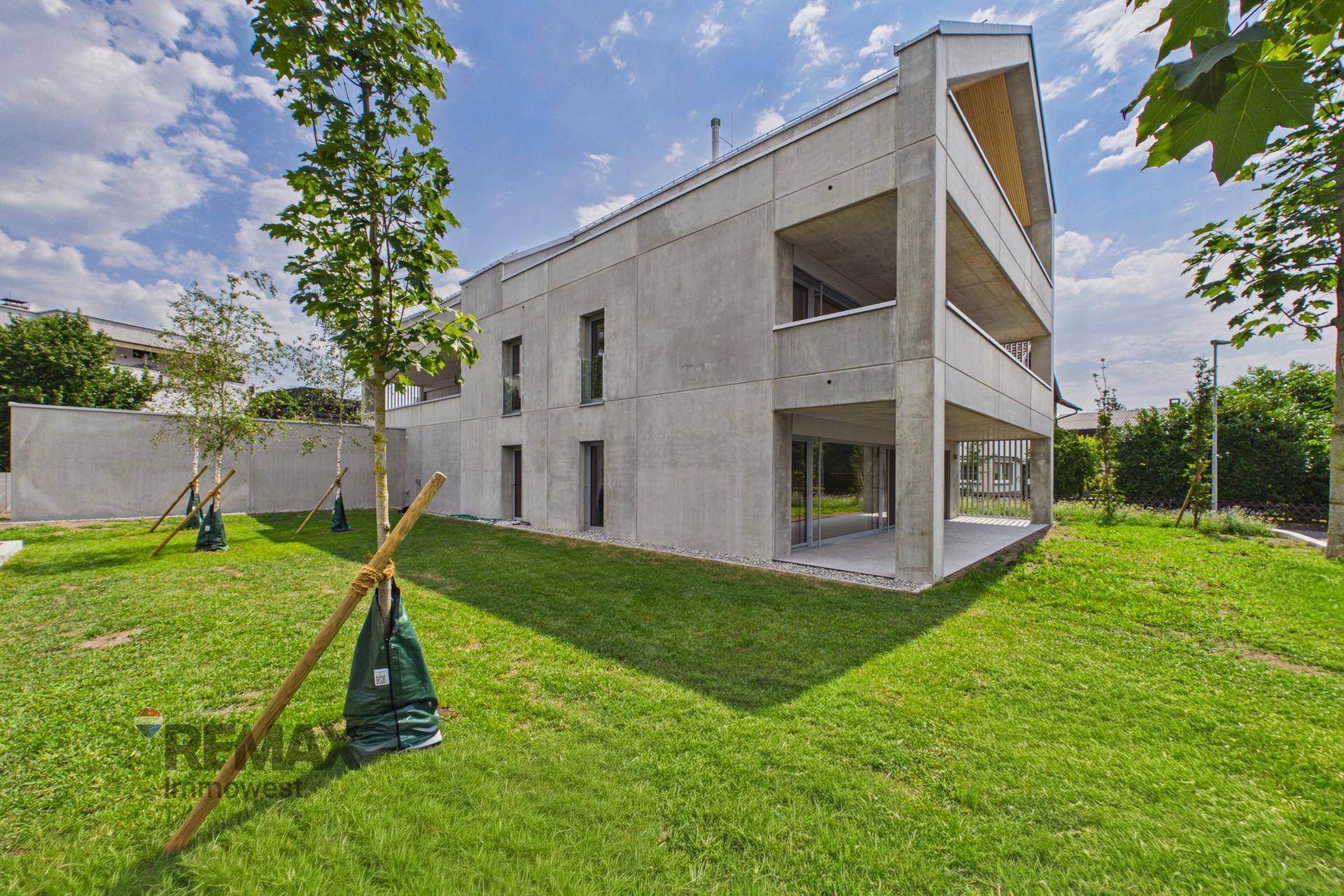Modernes Wohngebäude mit Betonfassade, großen Fenstern und gepflegtem Gartenbereich.