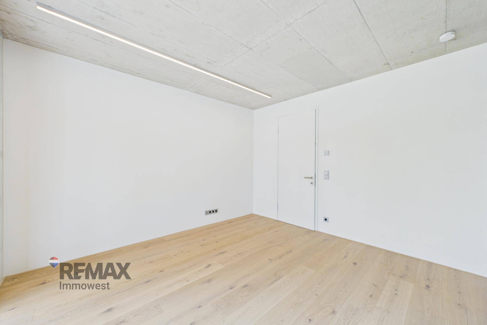 Modernes Zimmer mit Holzboden, weißen Wänden und schlichter Tür.