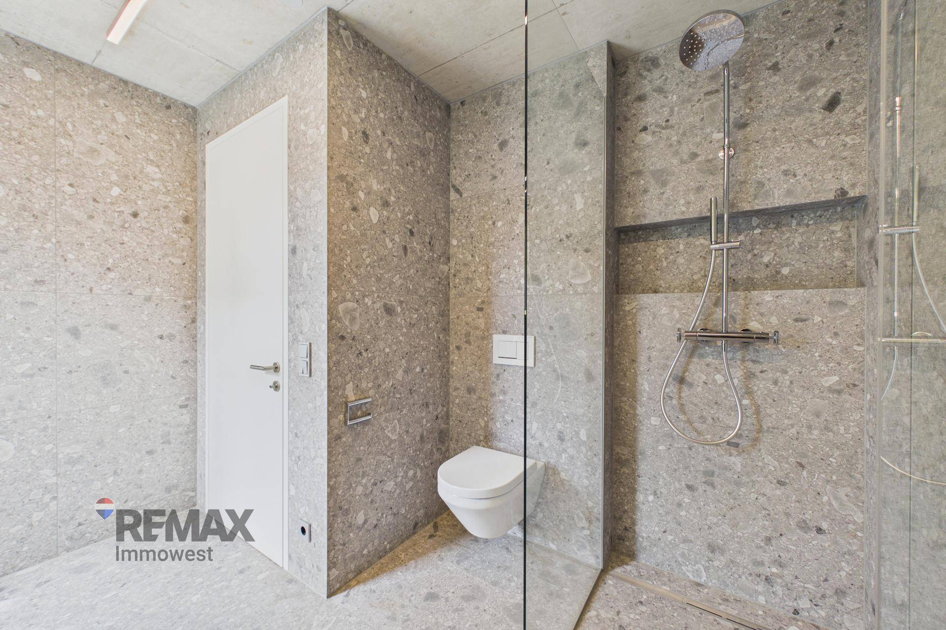 Modernes Badezimmer mit begehbarer Dusche, wandhängendem WC und grauen Fliesen.