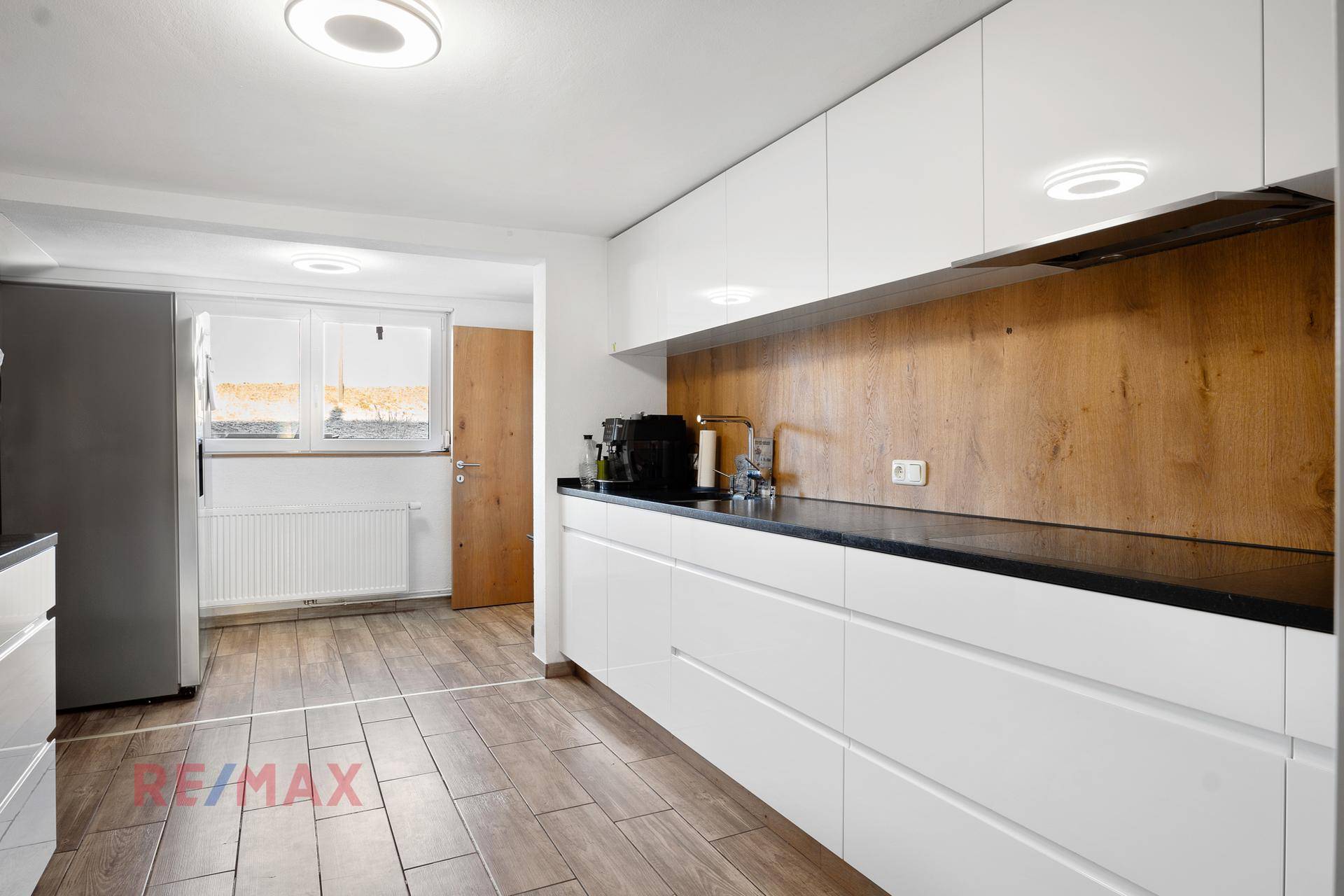 Moderne Küche mit weißen Hochglanzschränken, dunkler Arbeitsplatte und Fliesenboden.