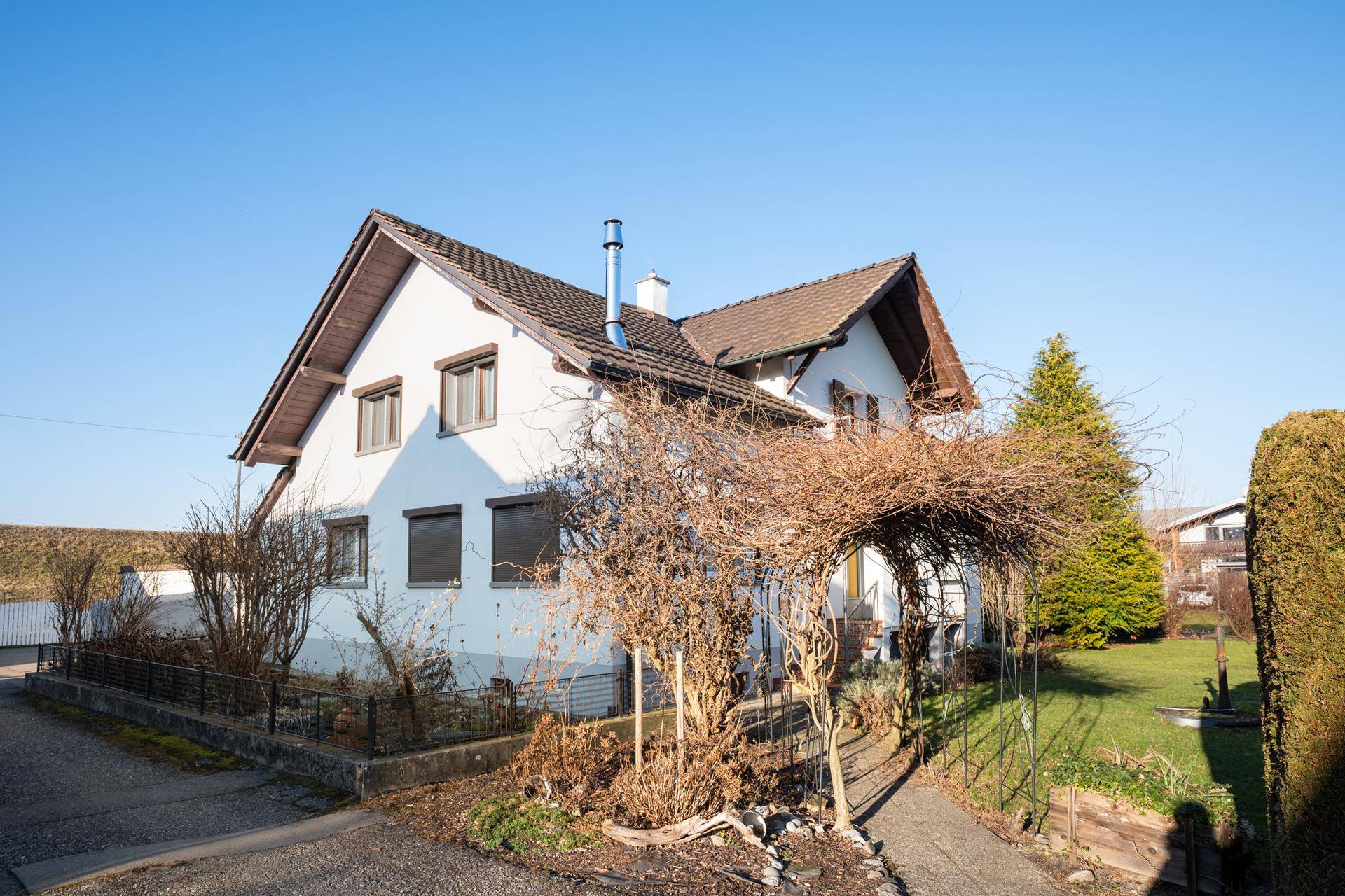 Ansicht eines Einfamilienhauses mit weißer Fassade, braunem Dach und einem kleinen Vorgarten.