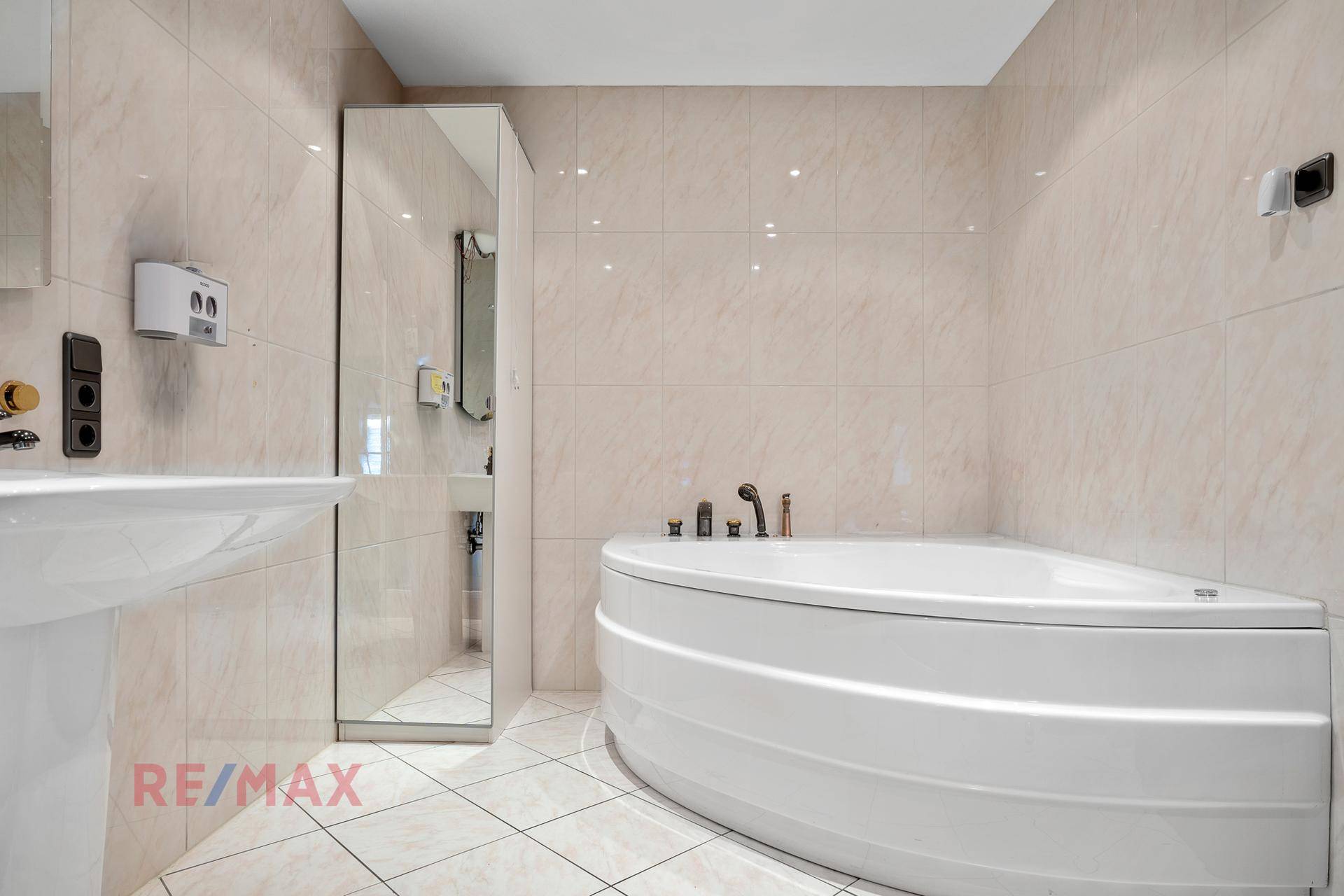Badezimmer mit beigefarbenen Fliesen, Eckbadewanne und einem großen Spiegel.