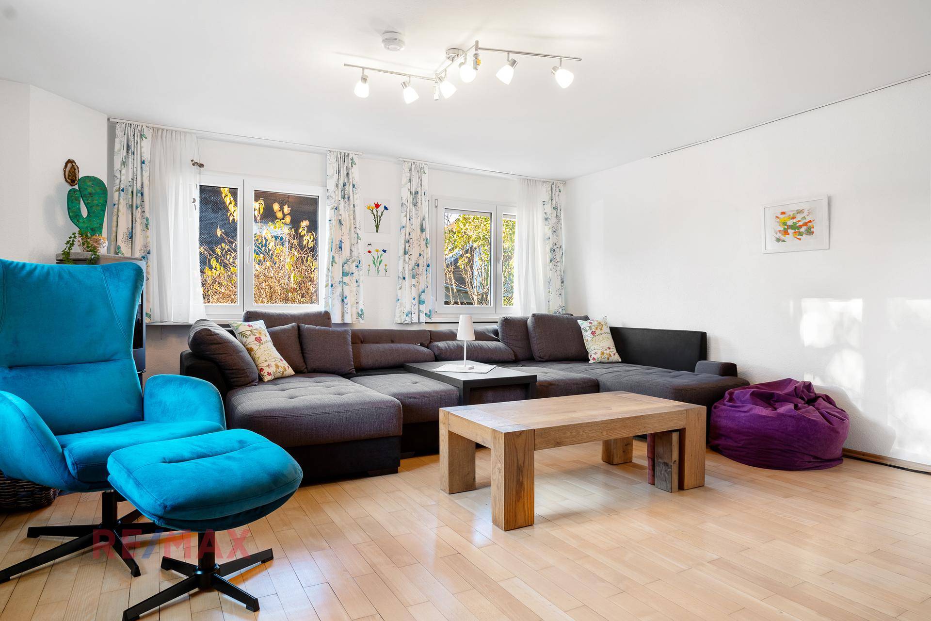 Helles Wohnzimmer mit großem Ecksofa, Holztisch und hellen Vorhängen an den Fenstern.