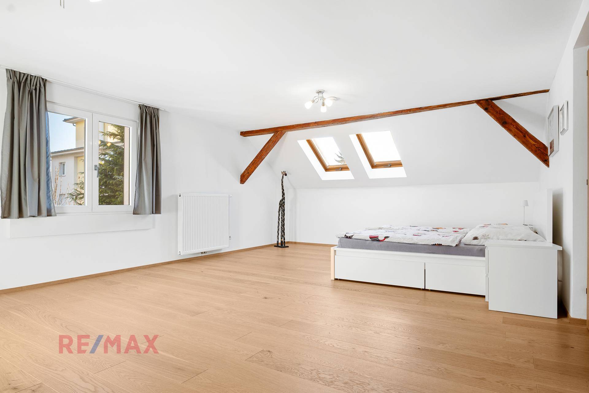 Helles Schlafzimmer im Dachgeschoss mit Holzboden, Dachfenstern und einem großen Fenster.