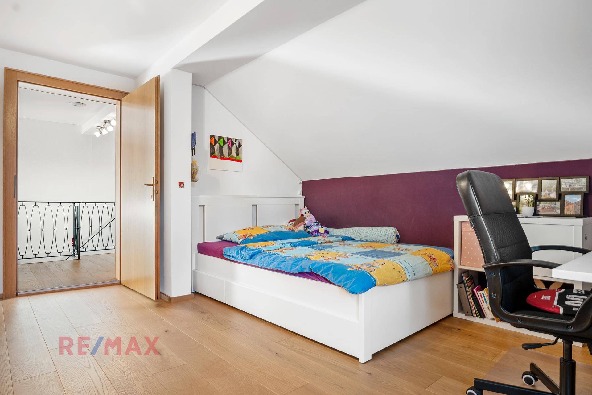 Kinderzimmer mit Holzboden, lila Akzentwand und Zugang zum Flur.